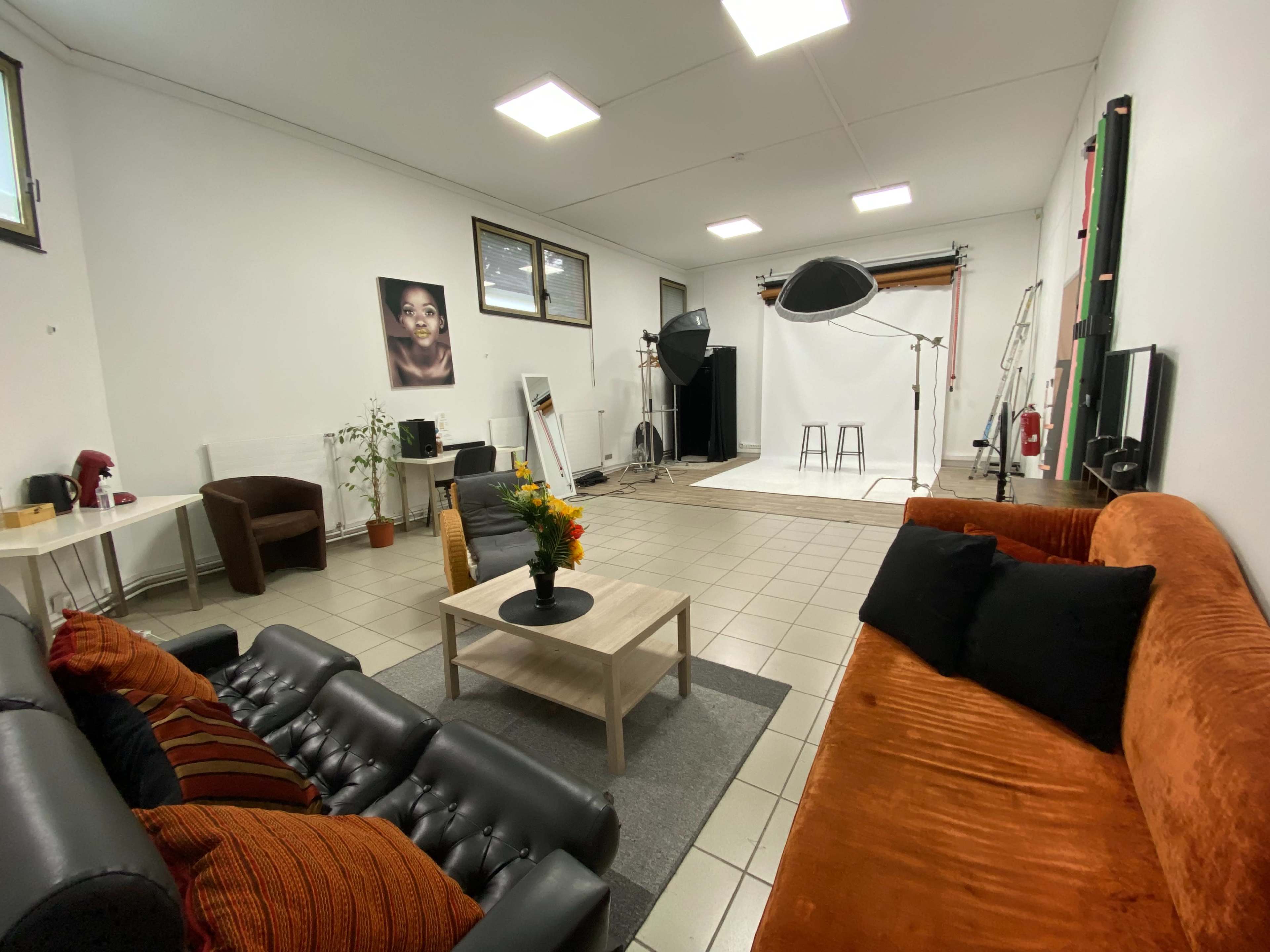 A spacious photography studio furnished with a seating area, a table with flowers, and a backdrop setup for photo shoots.