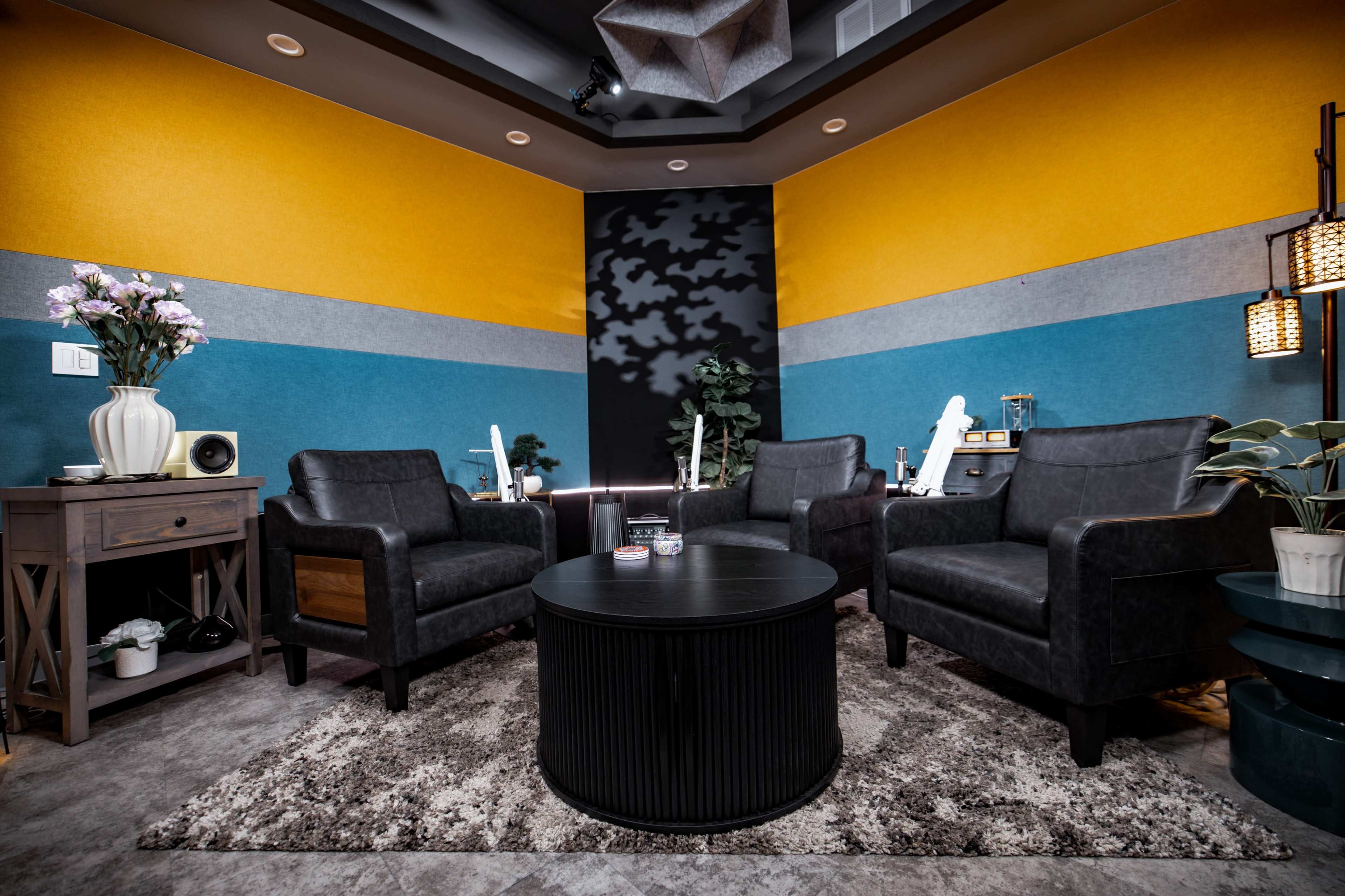 The image depicts a modern lounge area featuring two leather armchairs, a round black coffee table, and decorative plants against a backdrop of vibrant wall colors.