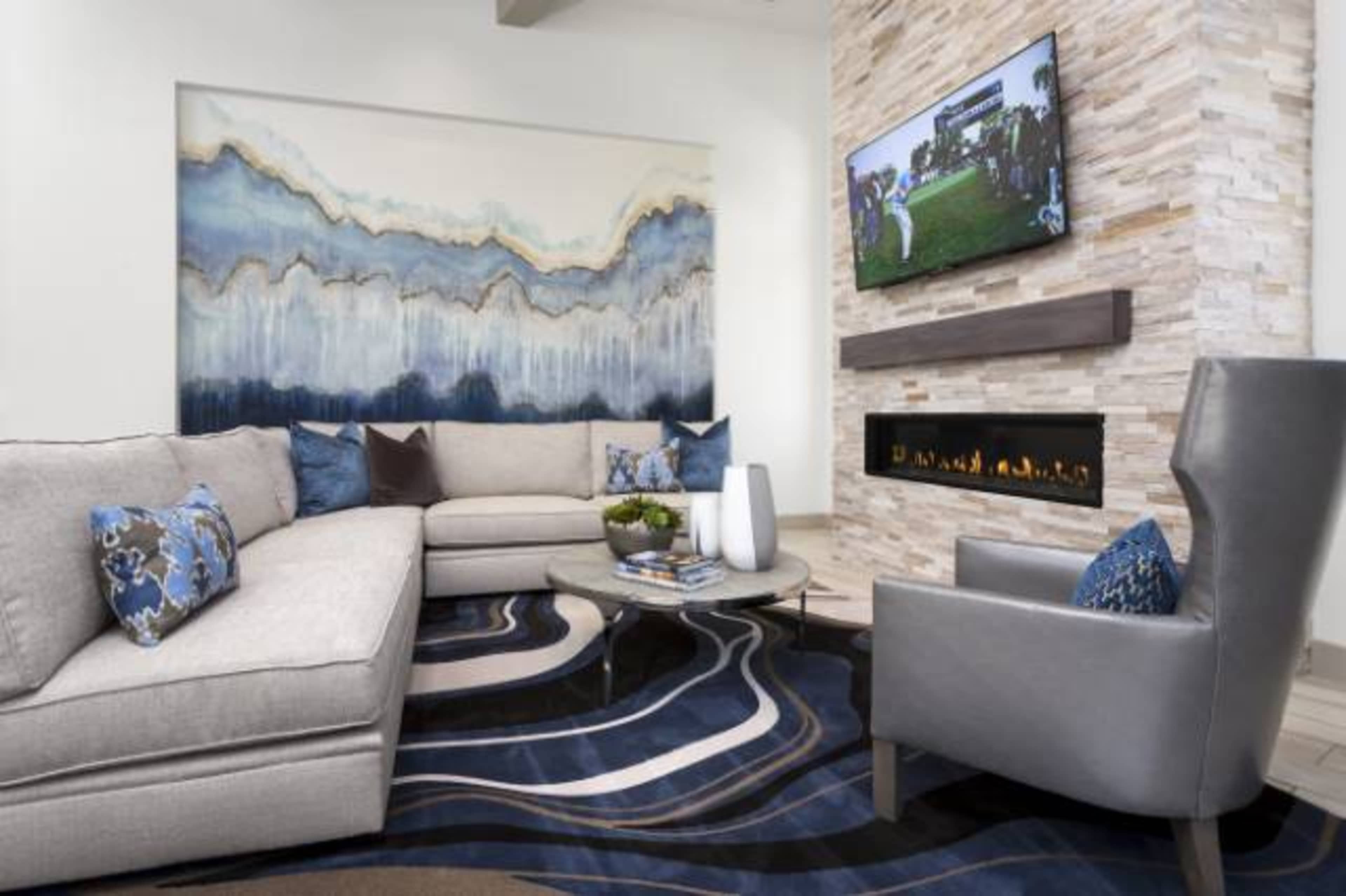 A modern living room with a sectional sofa, a wall-mounted television, and a stone fireplace, all complemented by abstract artwork and a patterned area rug.
