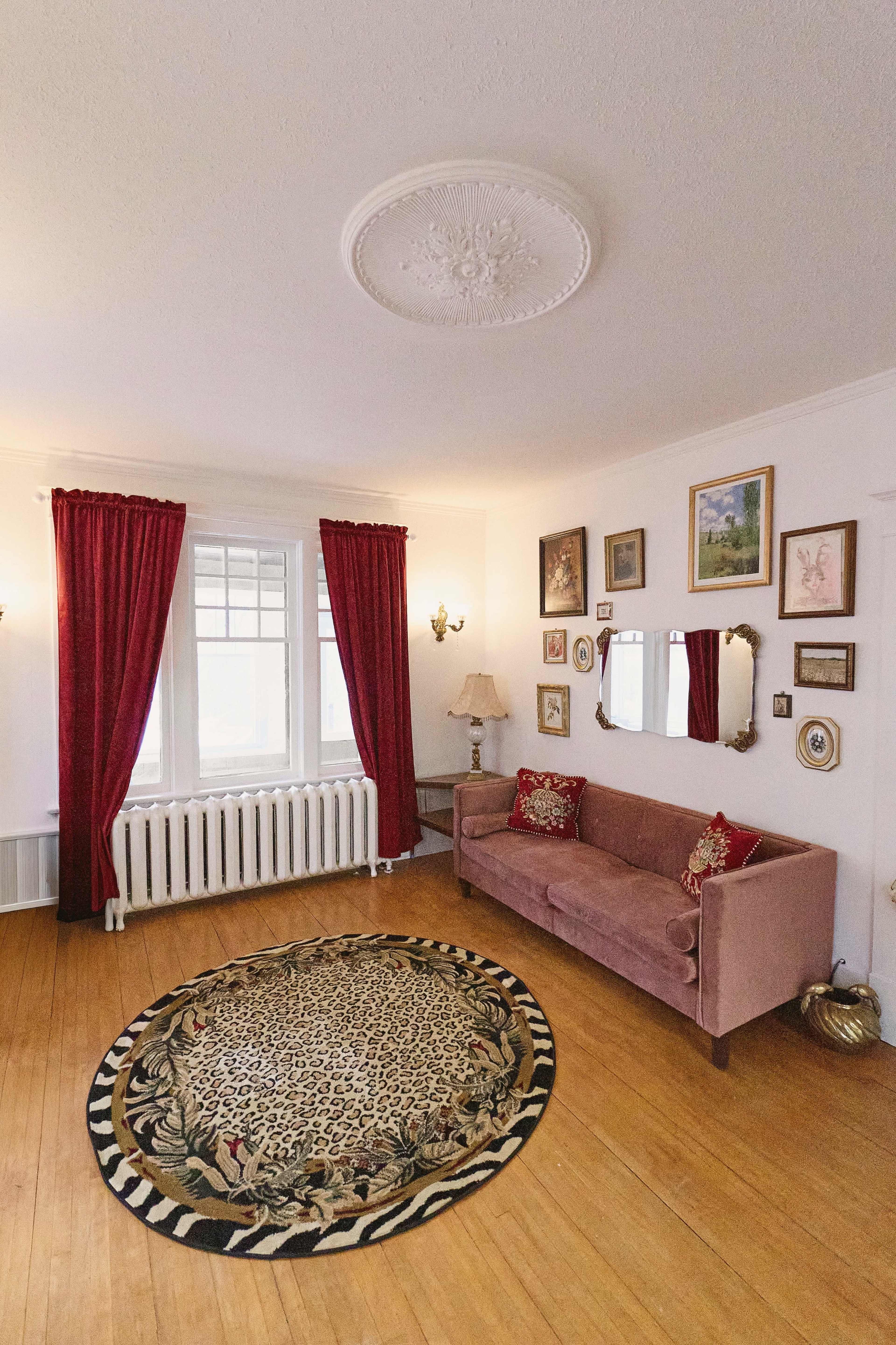 The room features a pink sofa, red curtains, a round leopard-patterned rug, and various framed artworks on the walls.