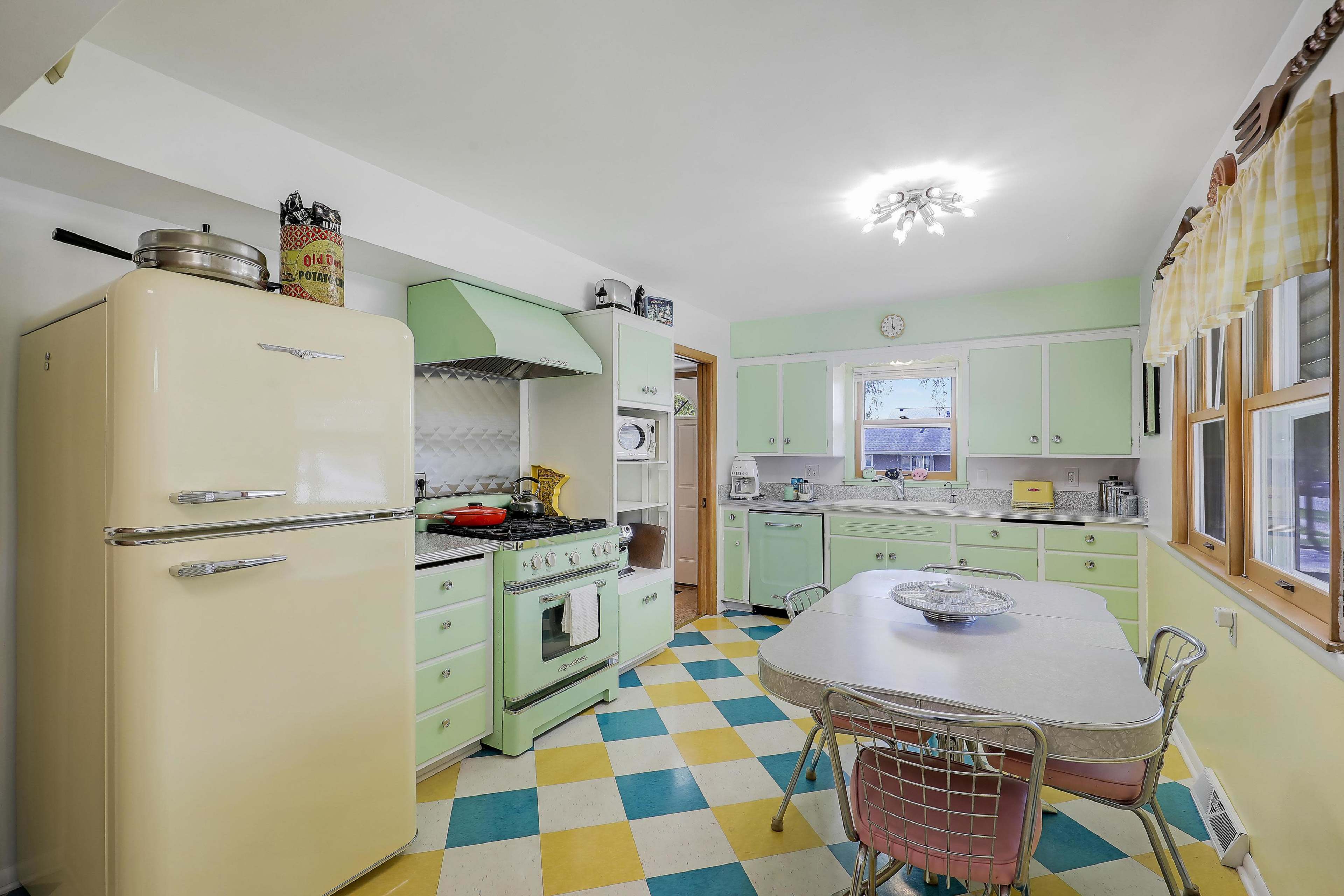The kitchen features retro-style mint green and cream cabinets, a vintage refrigerator, and a checkered floor of yellow and blue tiles.