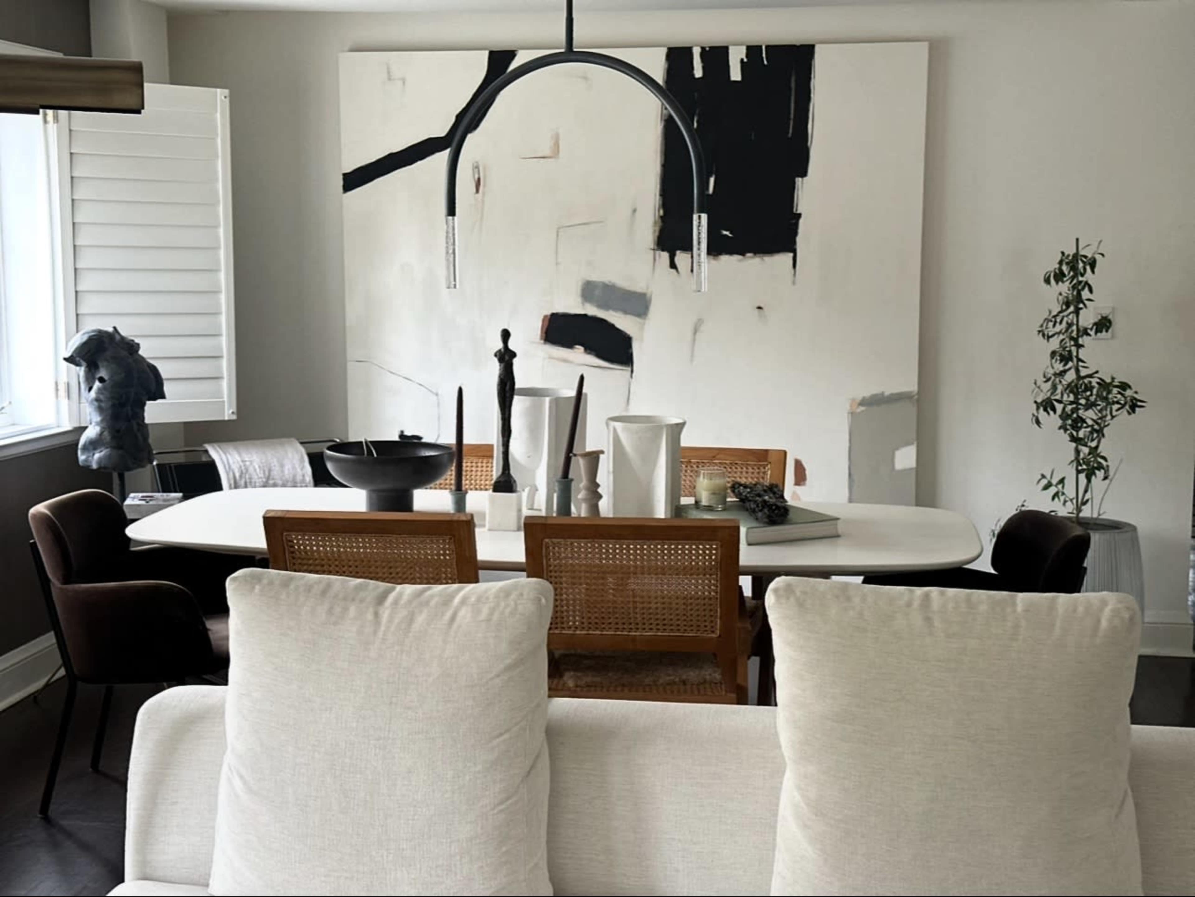 A dining area features a large white table surrounded by chairs, with a black and white abstract painting on the wall and decorative elements on the table.