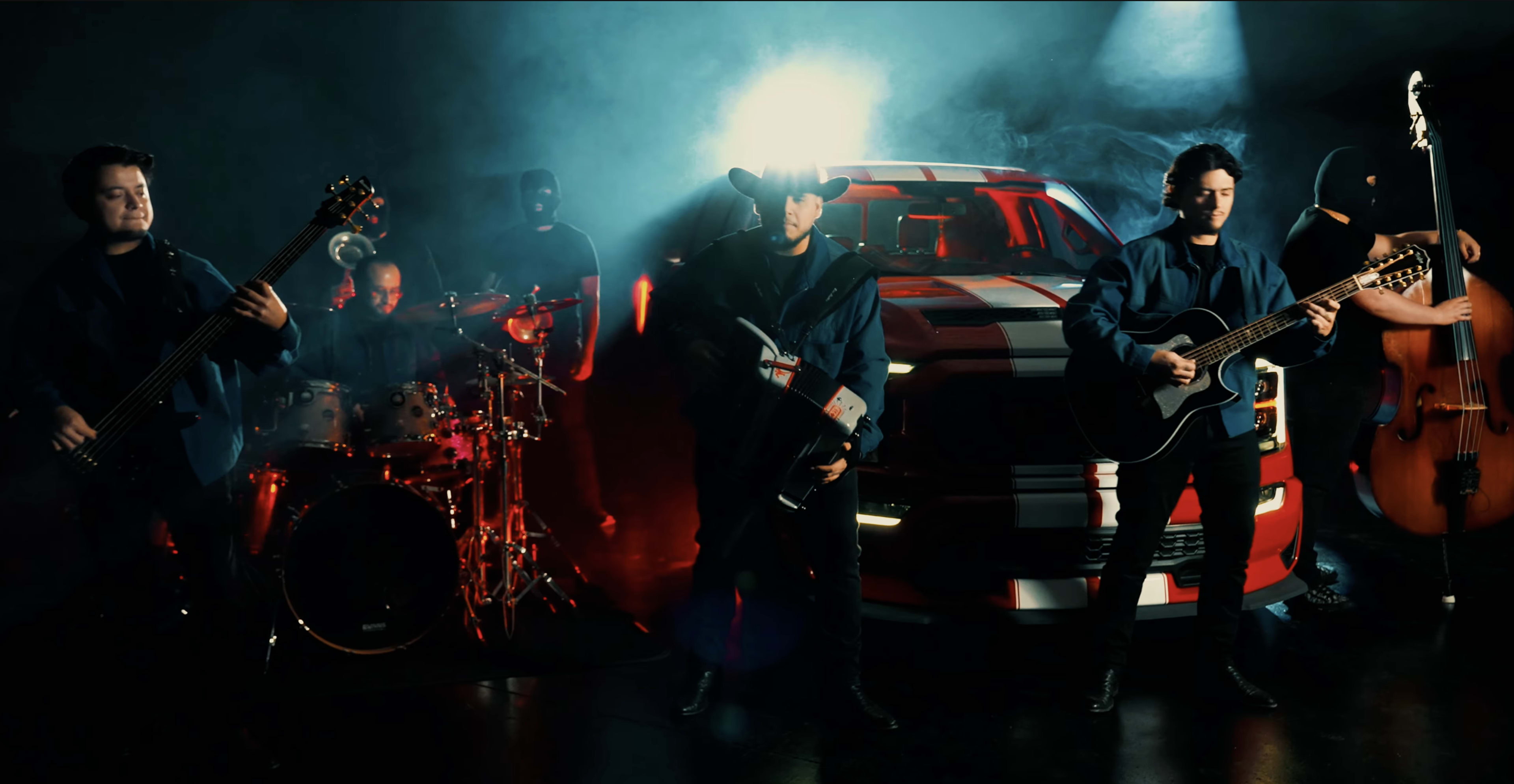 A band performs in front of a pickup truck, with dramatic lighting and smoke creating a dynamic atmosphere.