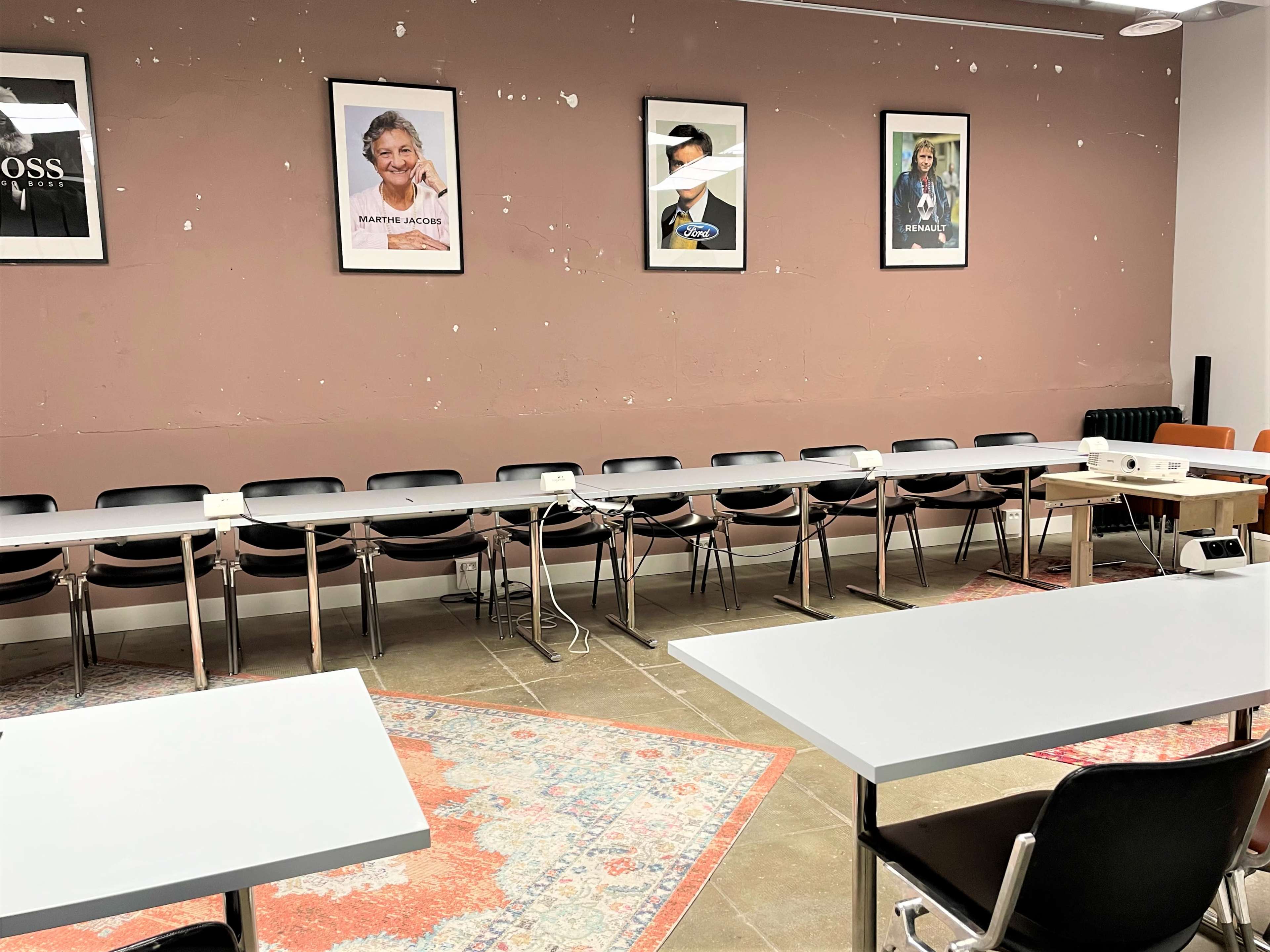 The room features several tables and chairs arranged in a row, with framed portraits hanging on the wall behind them.