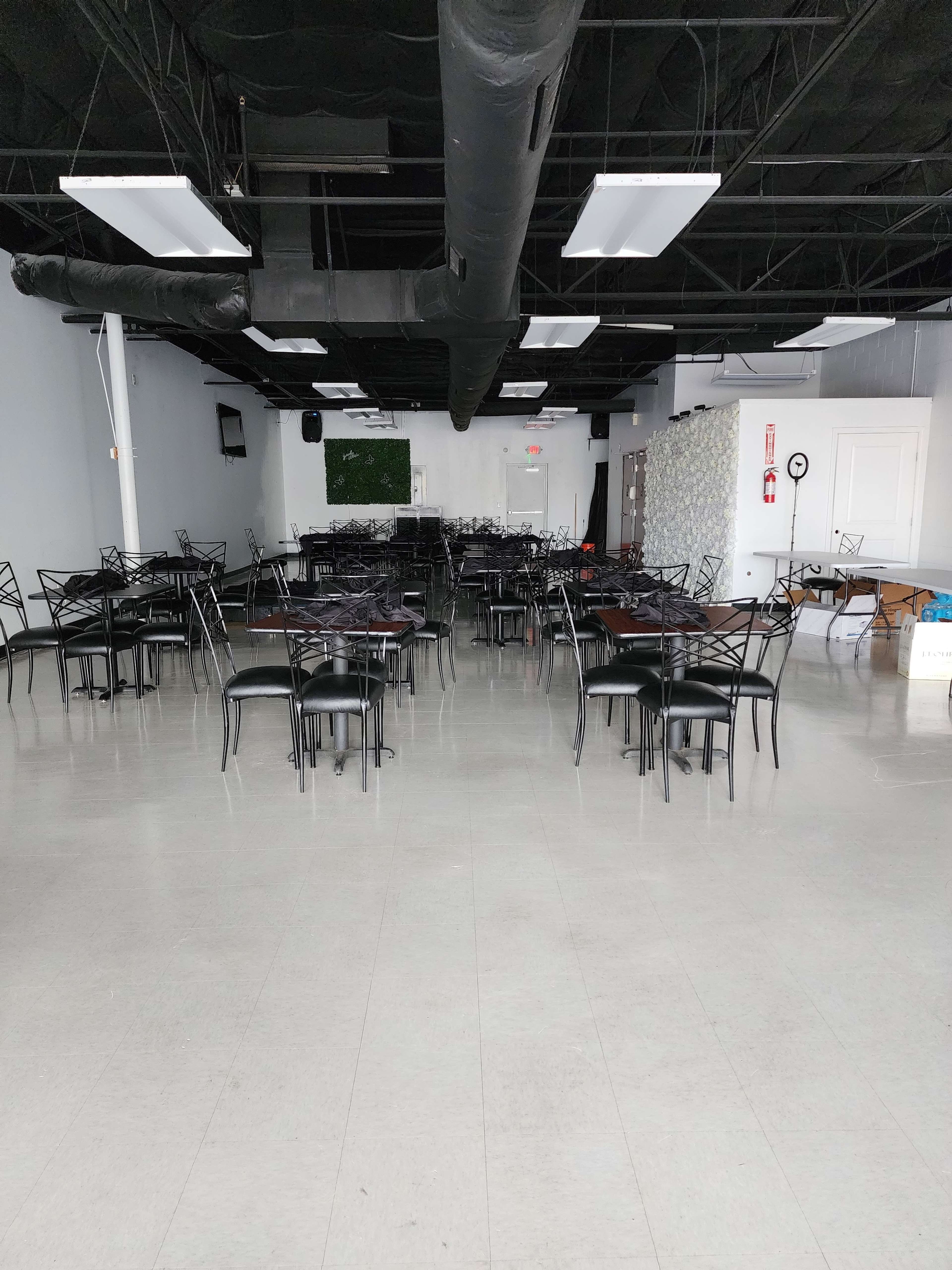 An empty dining area with several black chairs and tables arranged in rows on a light-colored floor.
