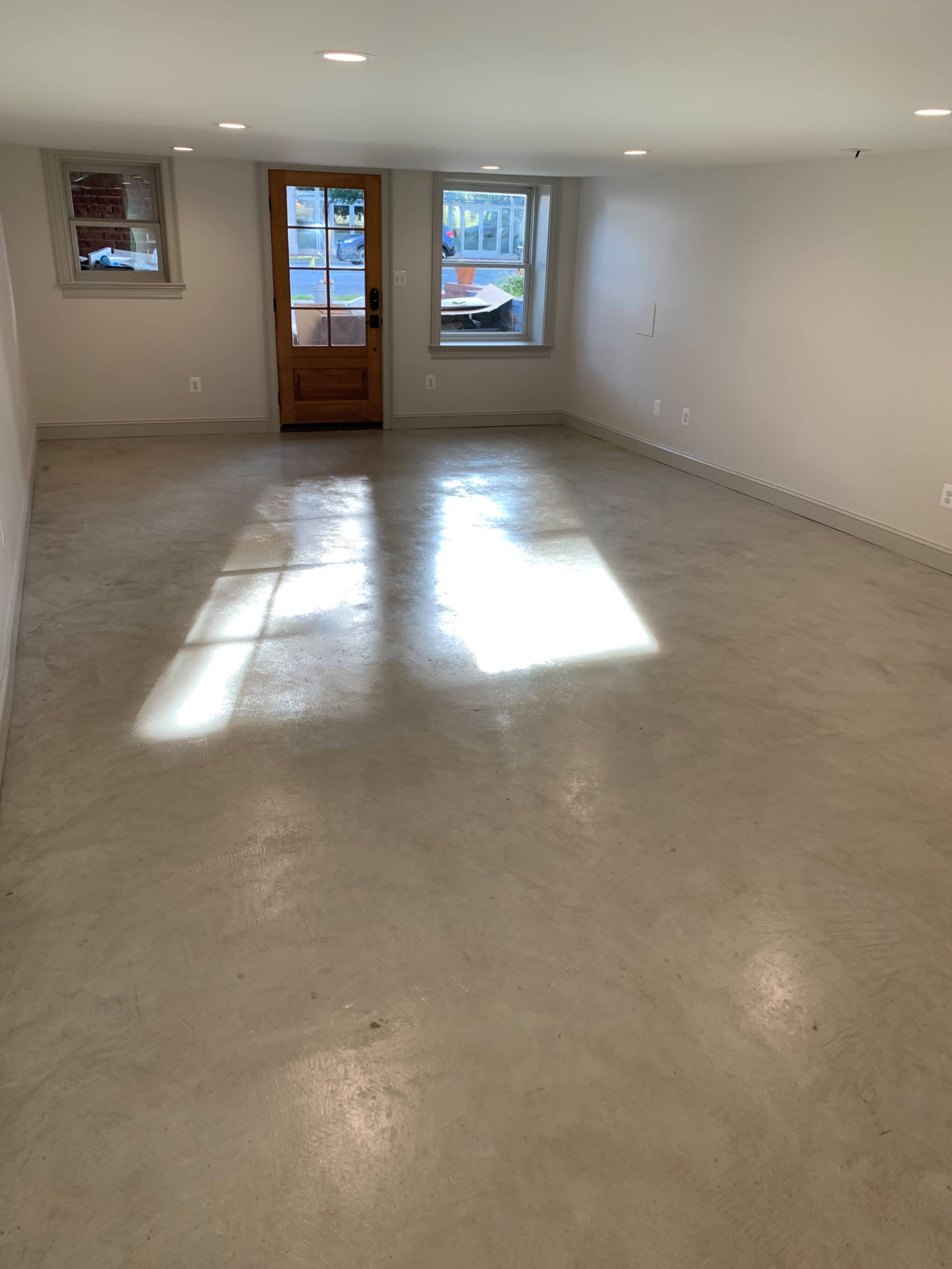 A spacious room with a concrete floor, featuring a door and a window that lets in natural light.