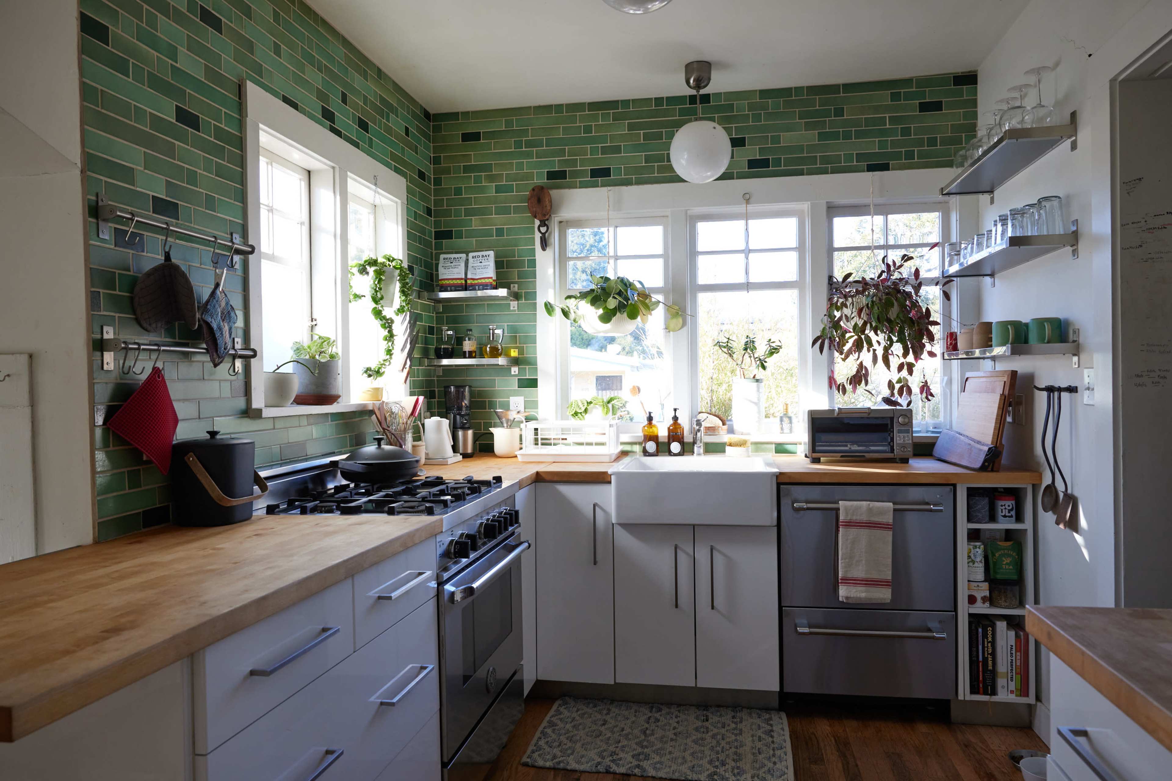 A modern kitchen with green tiled walls, a large window, and stainless steel appliances.