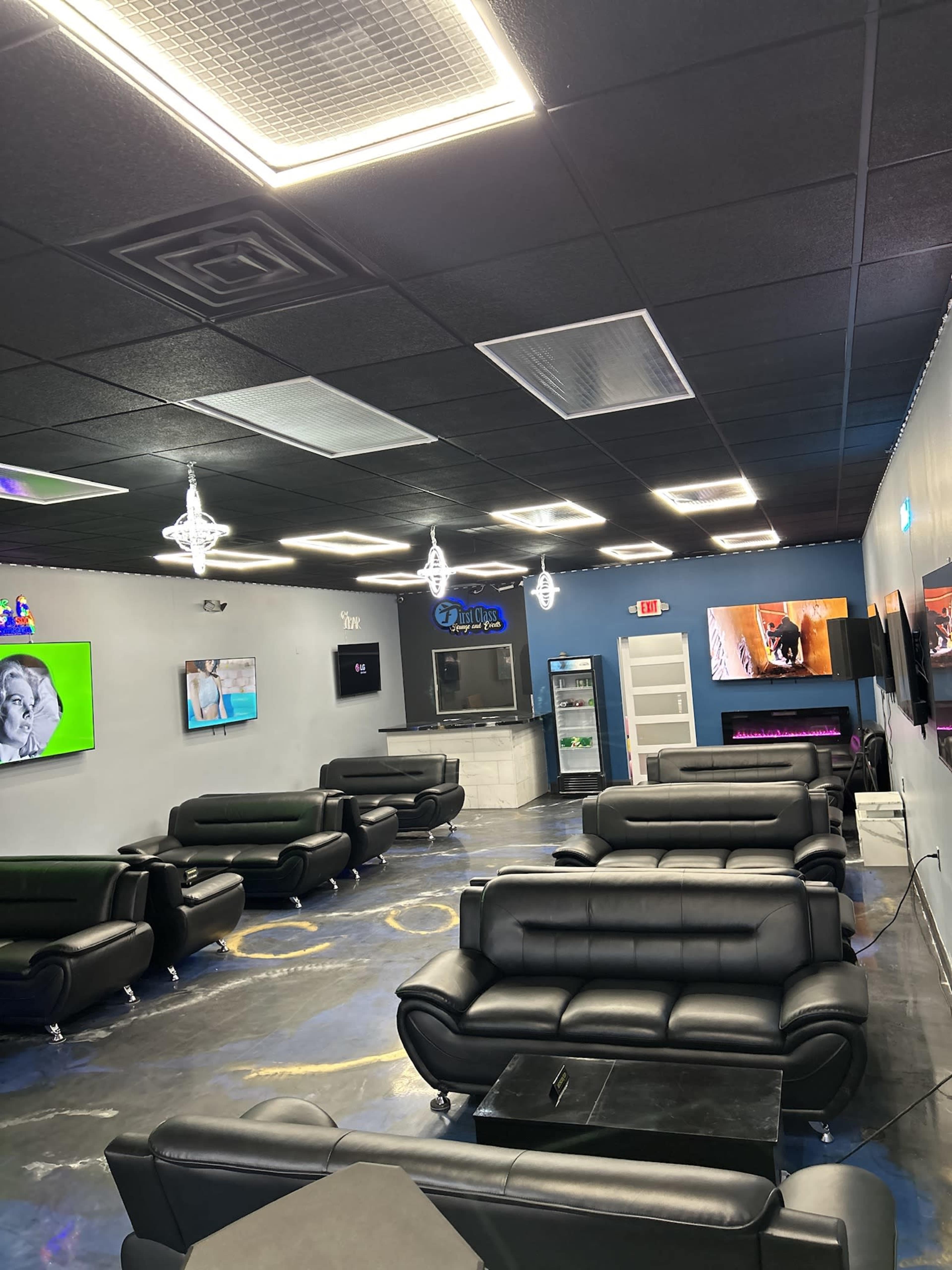 A modern lounge area featuring black sofas, multiple wall-mounted TVs, and a bar counter.