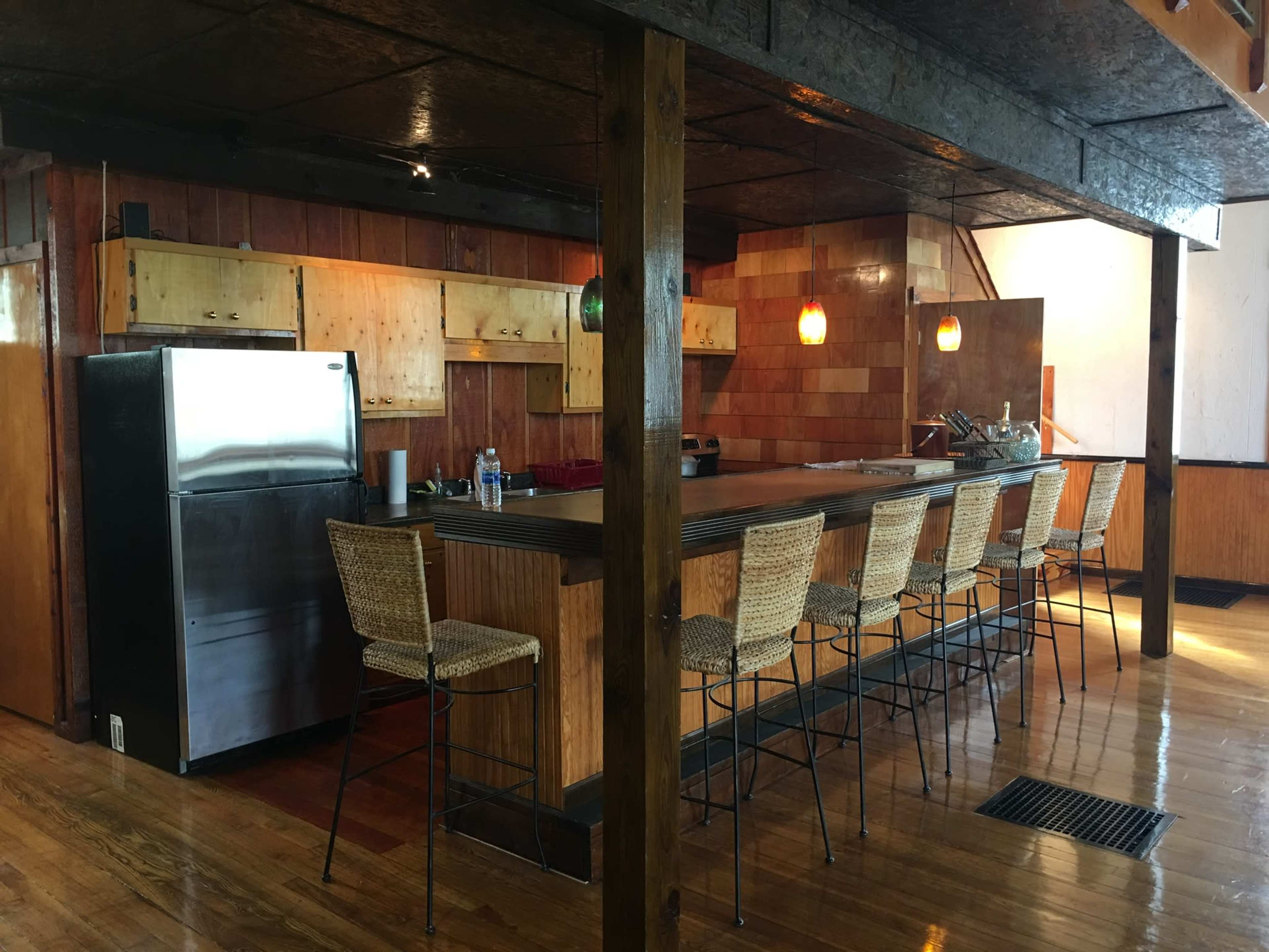 A modern kitchen with a long bar area featuring high stools, wooden cabinets, and a stainless steel refrigerator.