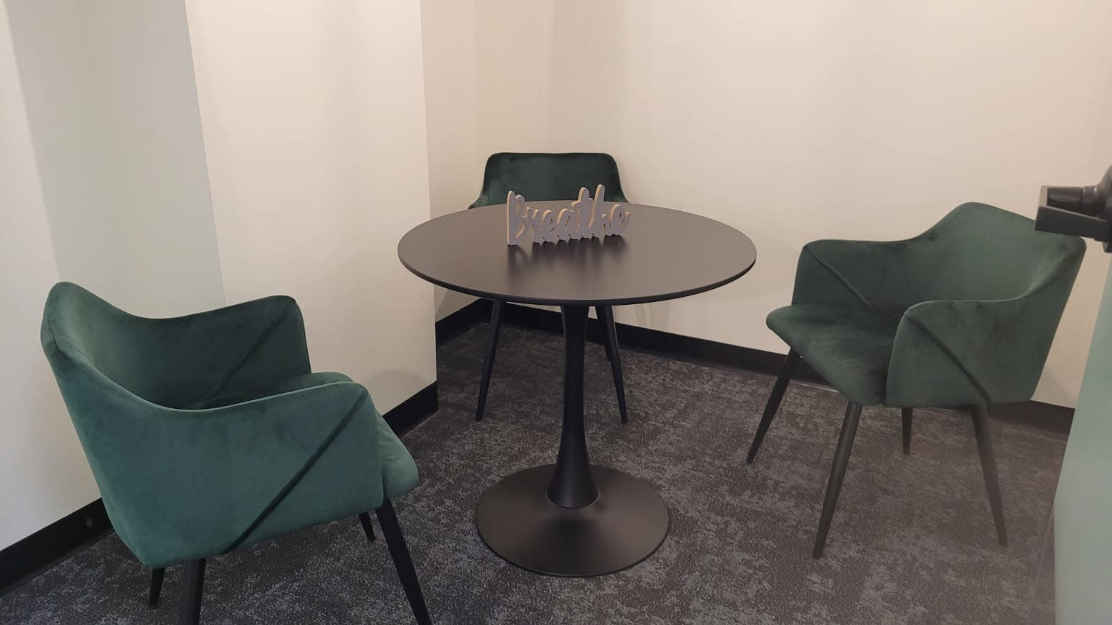 A small meeting area features a round black table surrounded by three green velvet chairs.