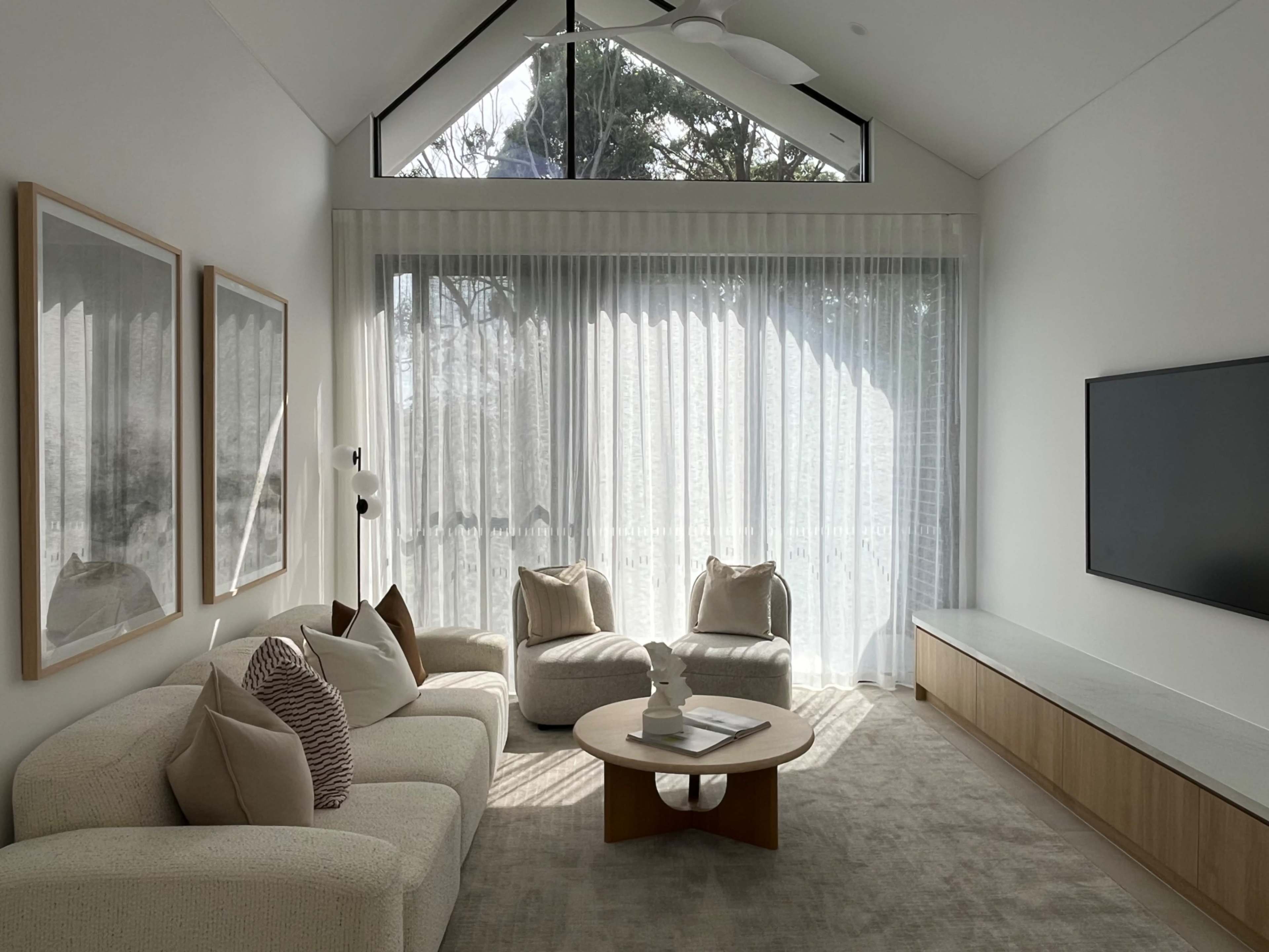 The room features a modern living area with large windows, soft furnishings, and a low coffee table.