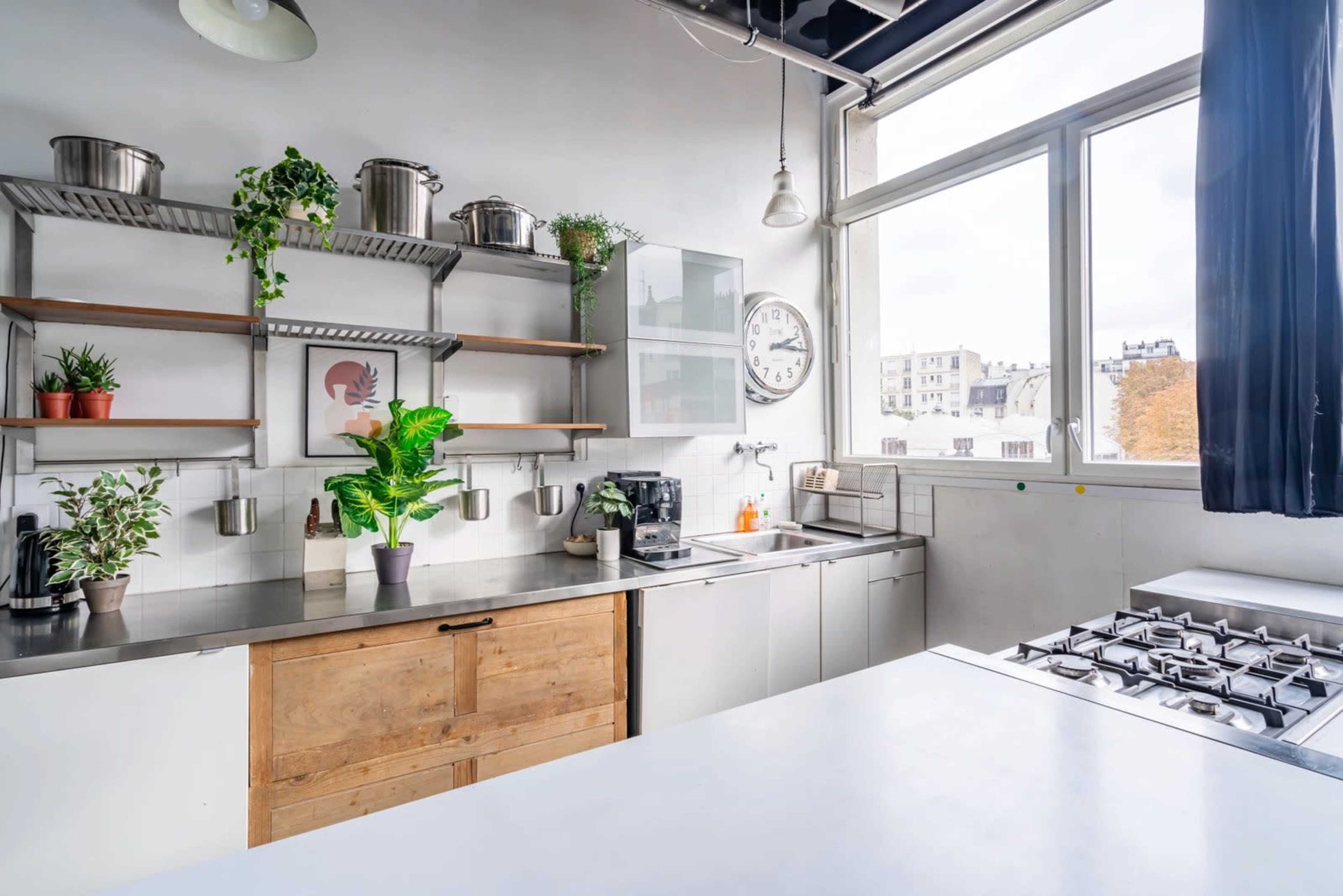 A modern kitchen features stainless steel countertops, wooden cabinetry, and large windows that provide natural light.
