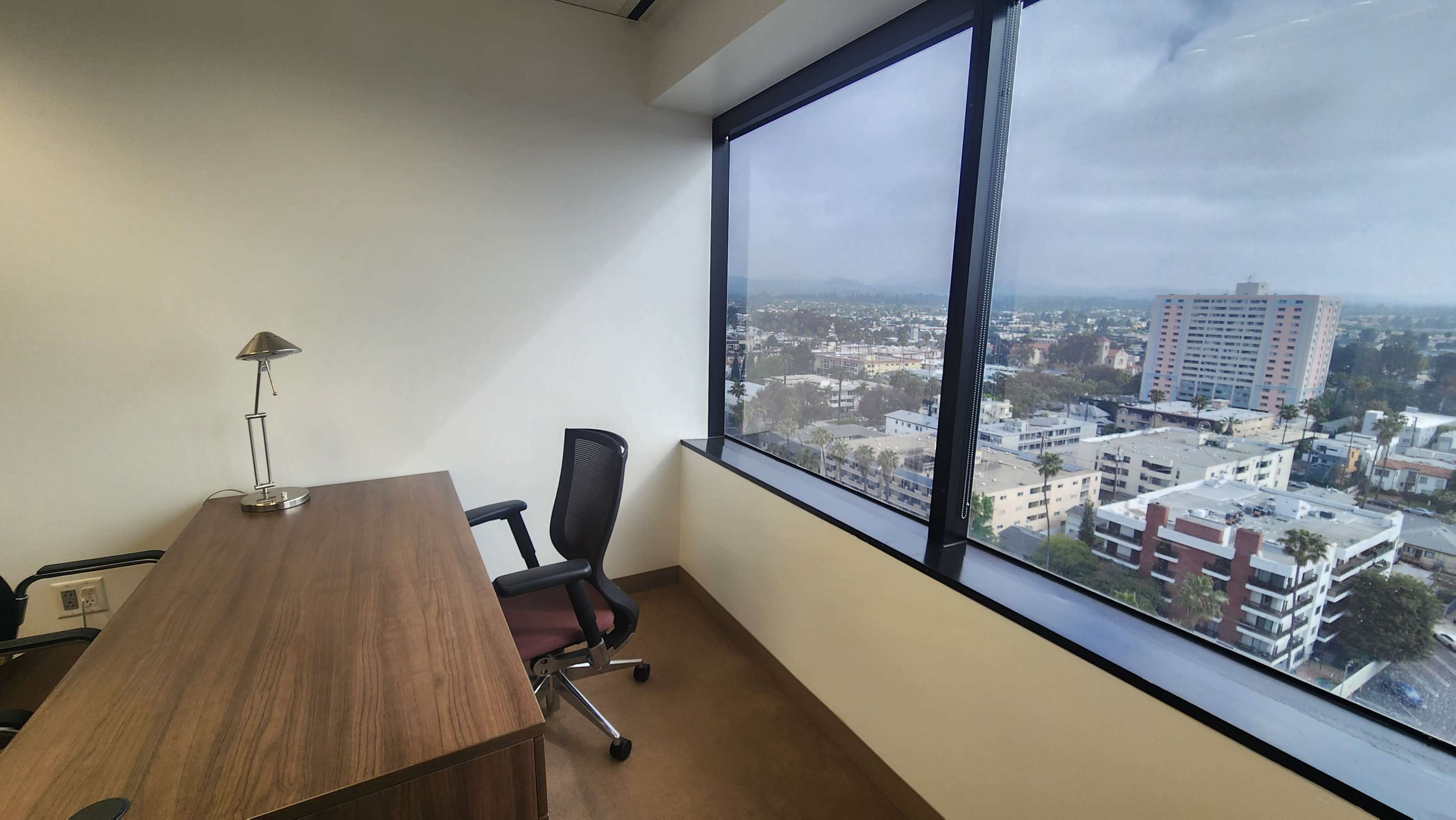 A modern office features a desk and chair positioned next to a large window overlooking a cityscape.