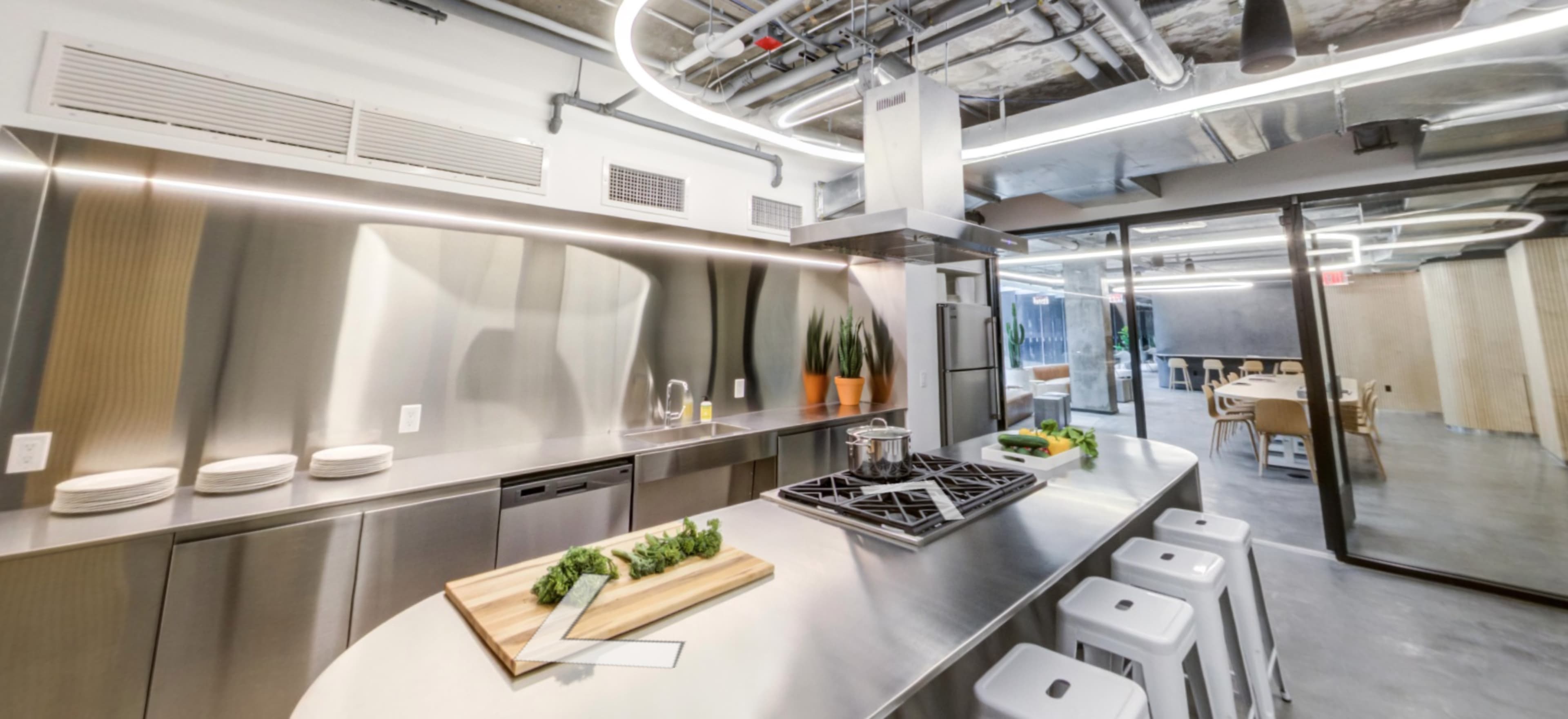 A modern kitchen with stainless steel appliances, a large island featuring a gas stove, and a dining area visible through a glass door.