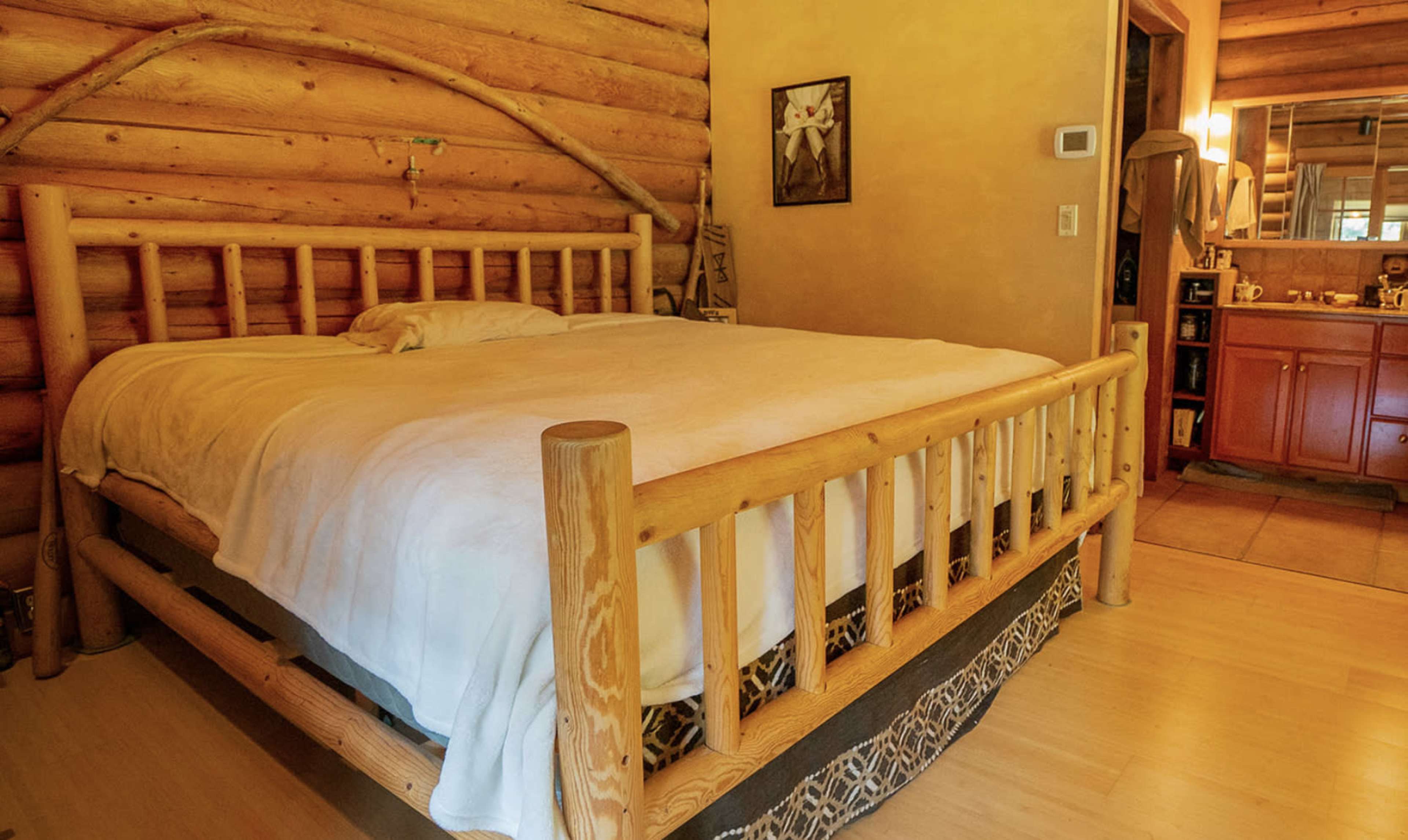 A rustic bedroom featuring a log cabin-style bed with a white comforter and wooden walls.