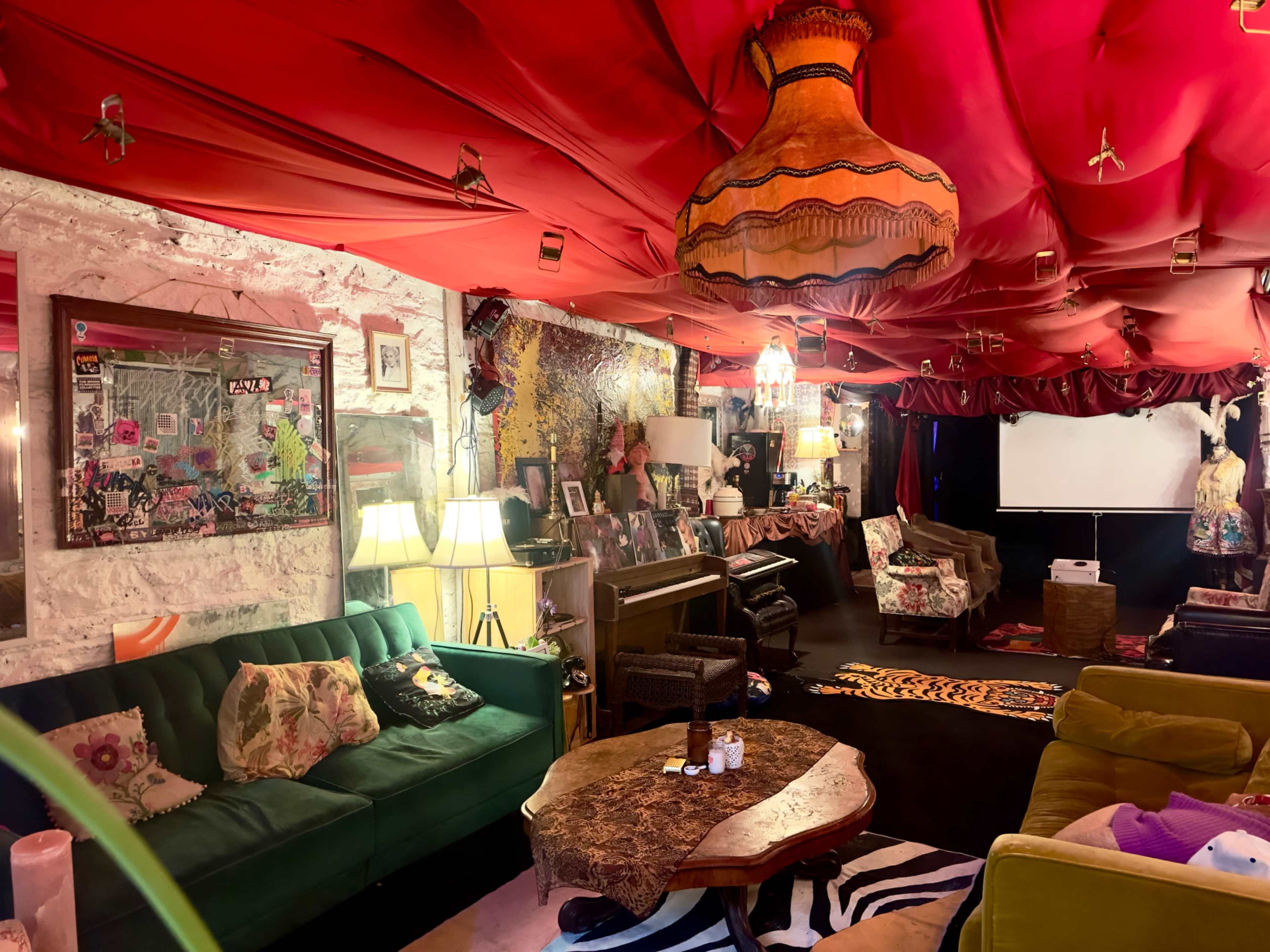 The image depicts a colorful lounge area adorned with a vibrant red ceiling, eclectic decor, plush seating, and various artistic elements.