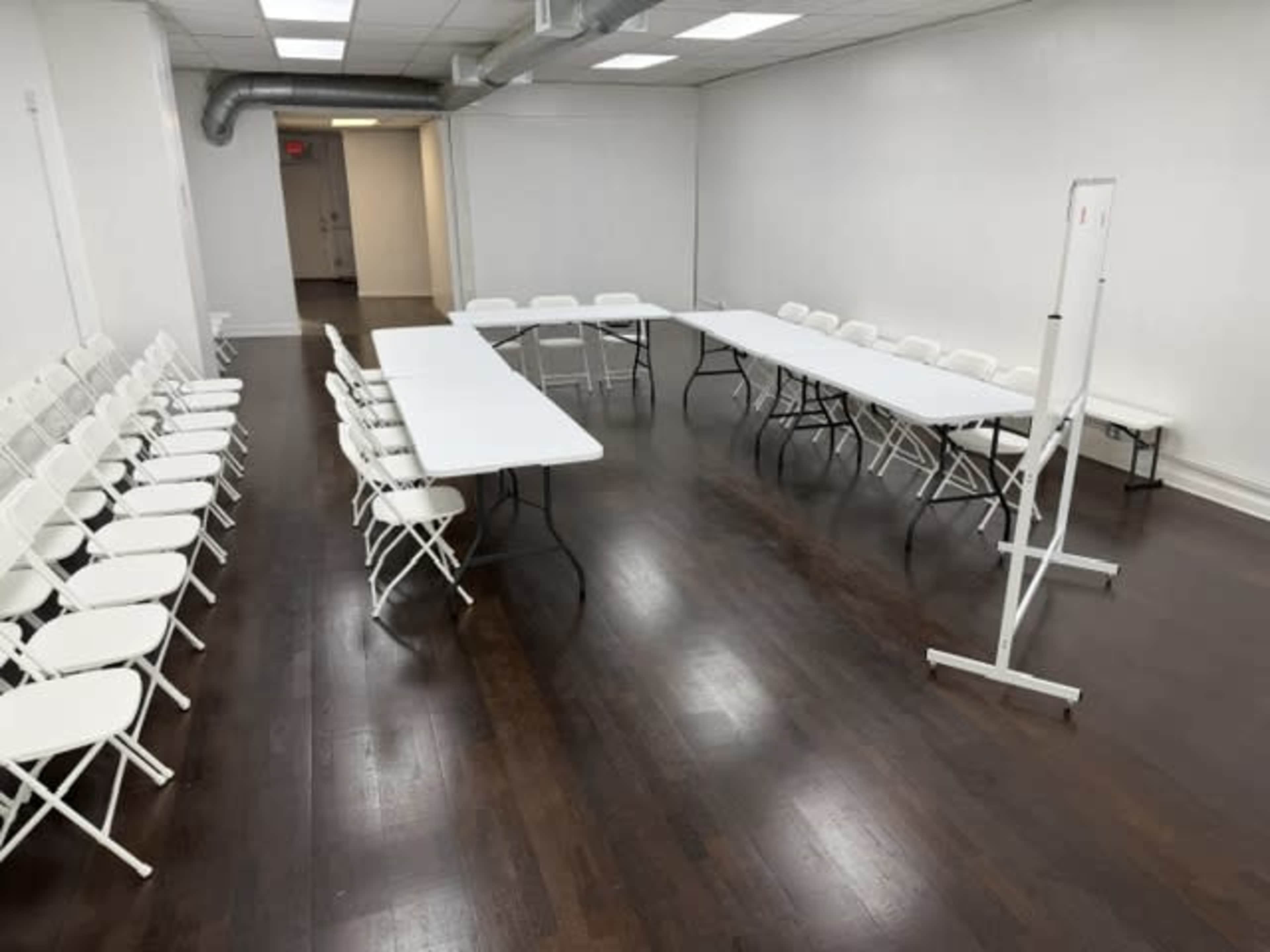 A spacious room features two rows of folding chairs on one side and a series of tables arranged in a U-shape on the other.