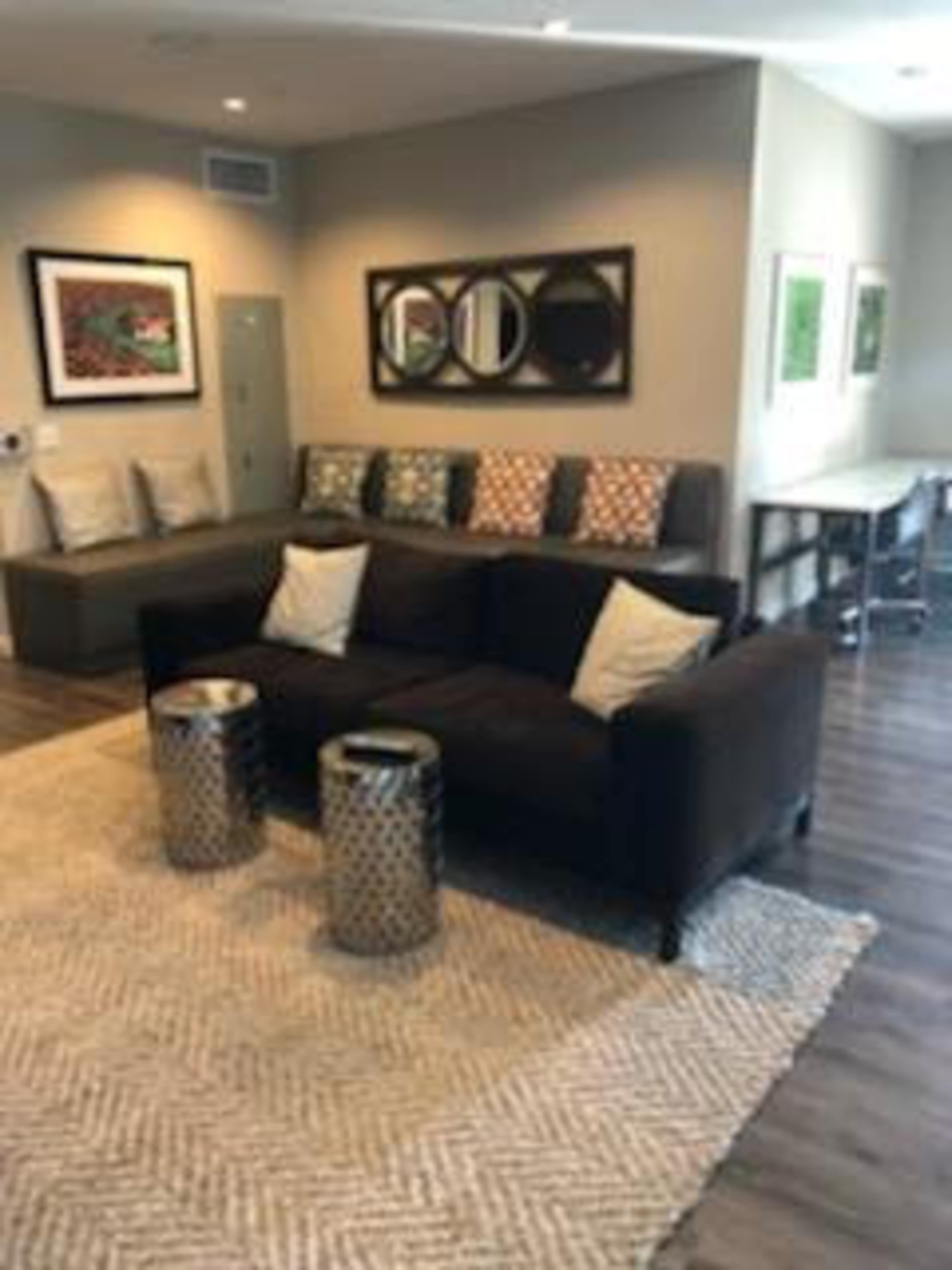 The image shows a modern living area with a dark brown sofa, decorative pillows, two metallic side tables, and a textured rug on a wooden floor.