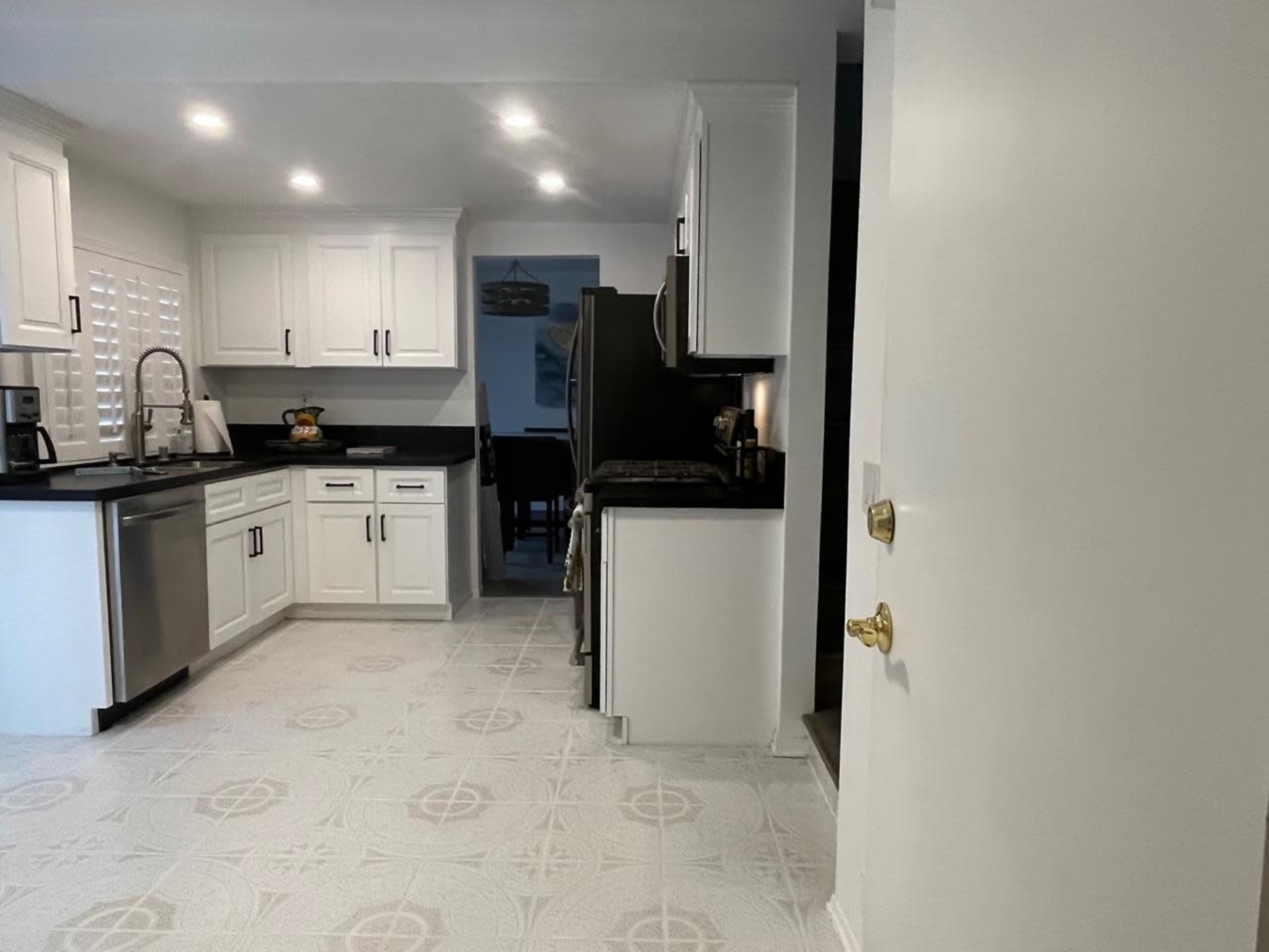 A modern kitchen features white cabinetry, black countertops, and a tiled floor.