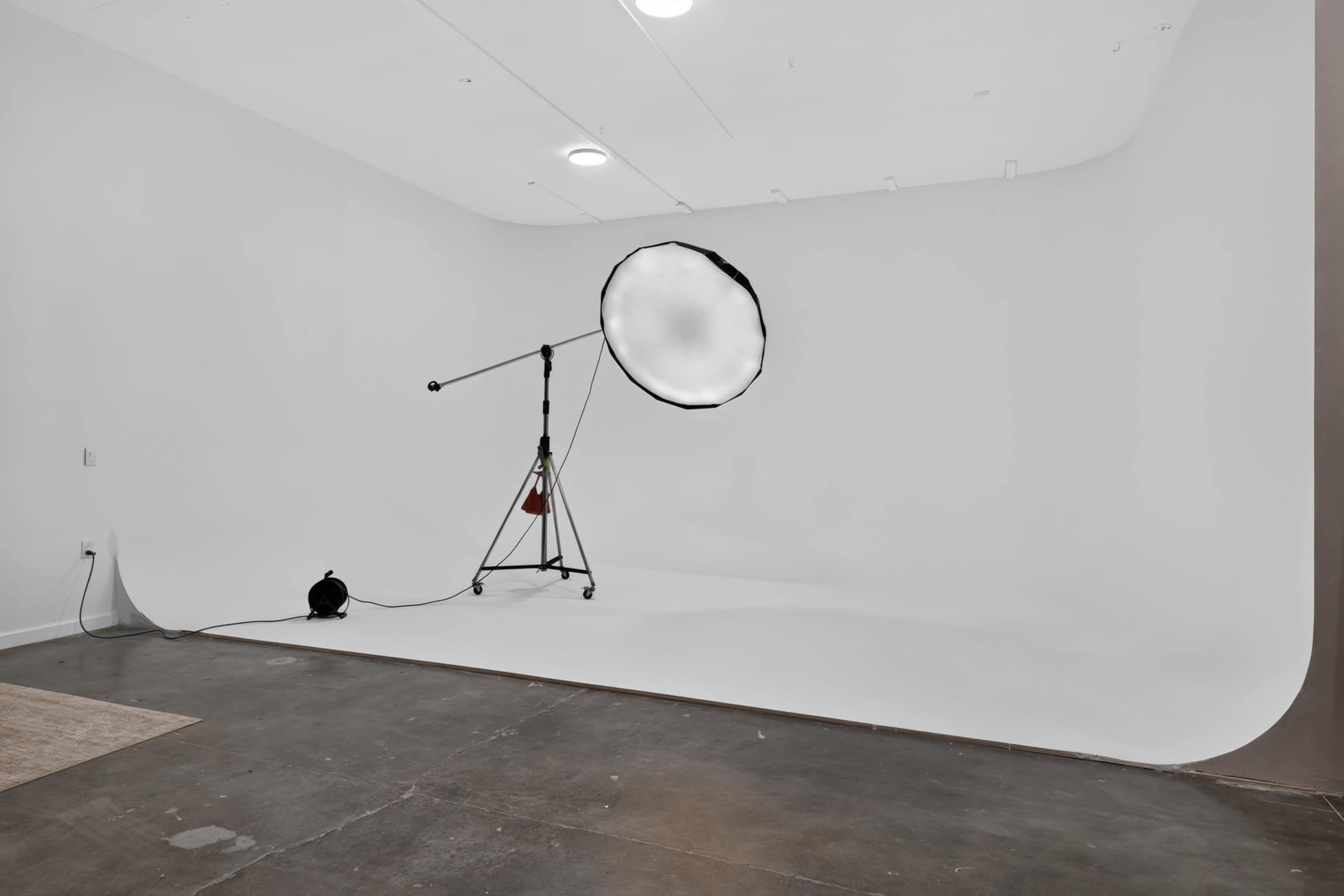 The image shows a photography studio with a seamless white backdrop and a large softbox light on a stand.
