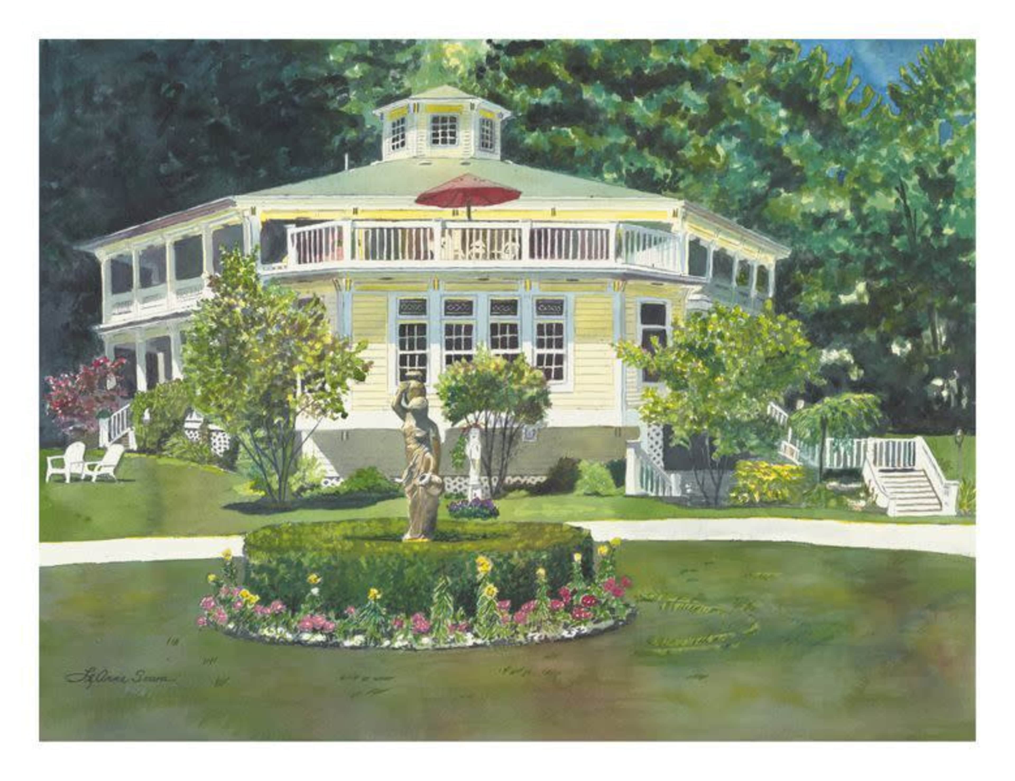 A large yellow house with a wraparound porch, surrounded by greenery and colorful flower beds, with a central statue in a neatly trimmed hedge garden.