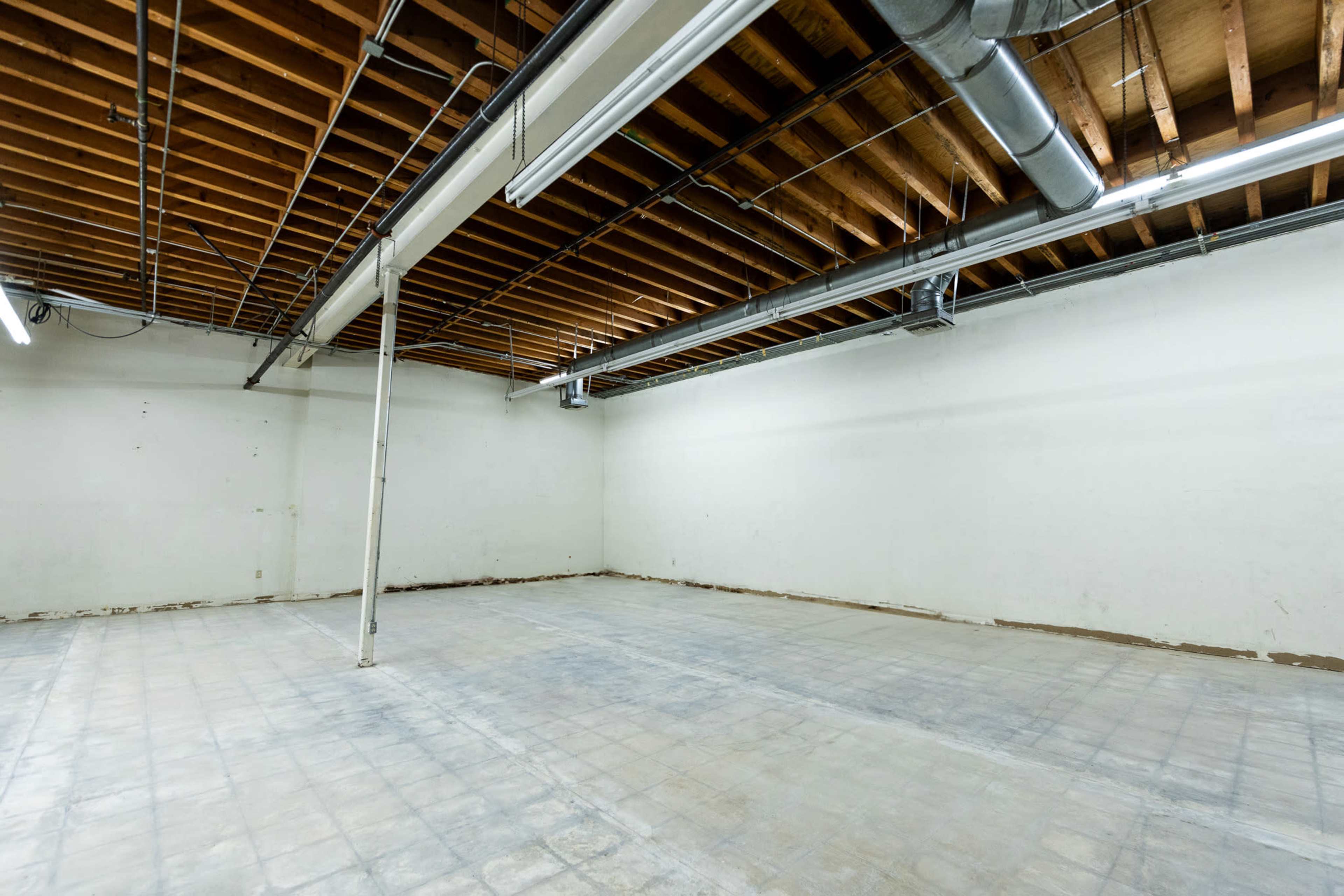 The image shows an empty room with a bare concrete floor and exposed wooden beams on the ceiling.