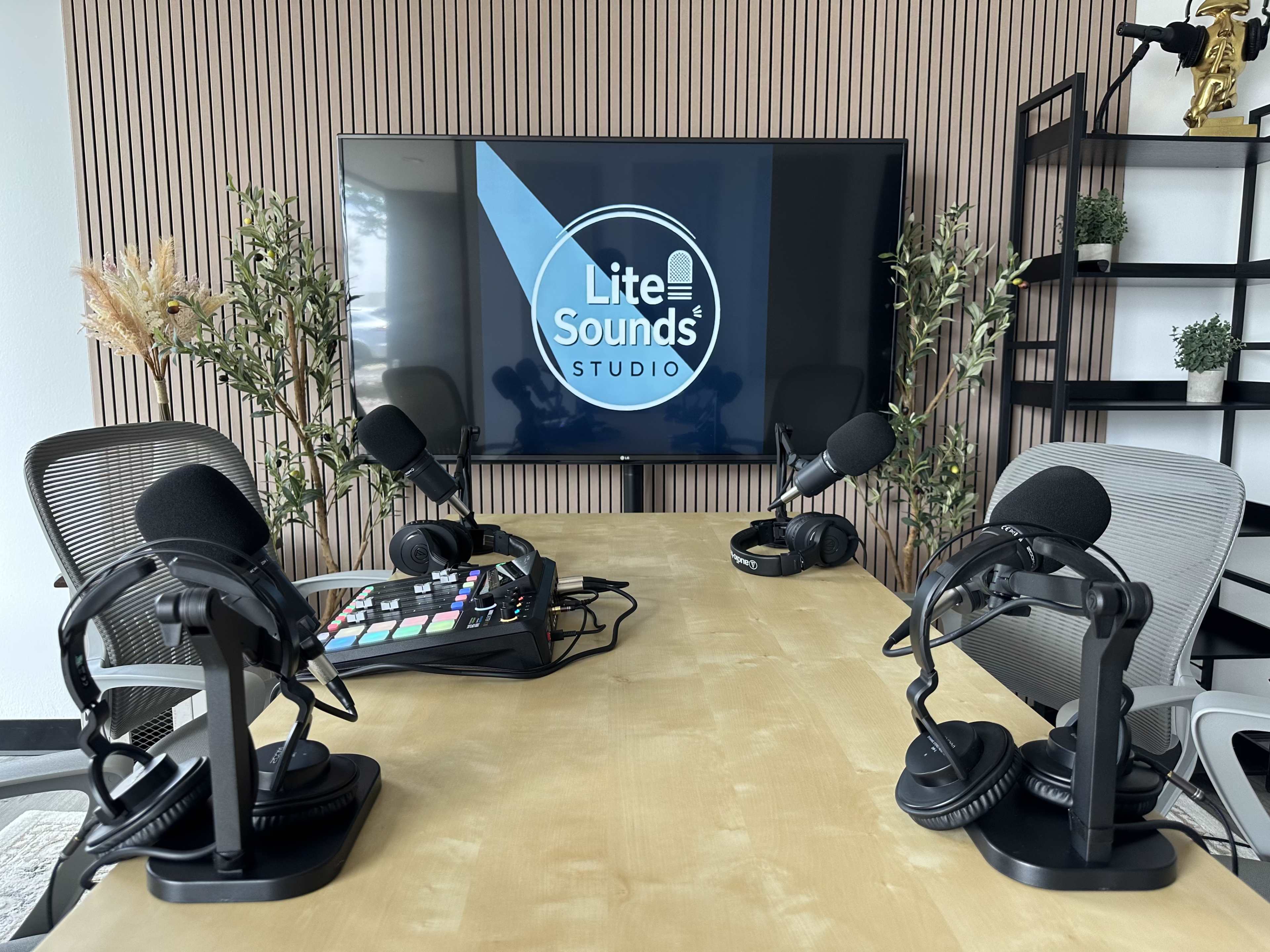 The image shows a modern podcast studio featuring a large screen displaying the "Lite Sounds Studio" logo, a table with four microphones, headphones, and audio equipment, set against a backdrop of wooden paneling and greenery.