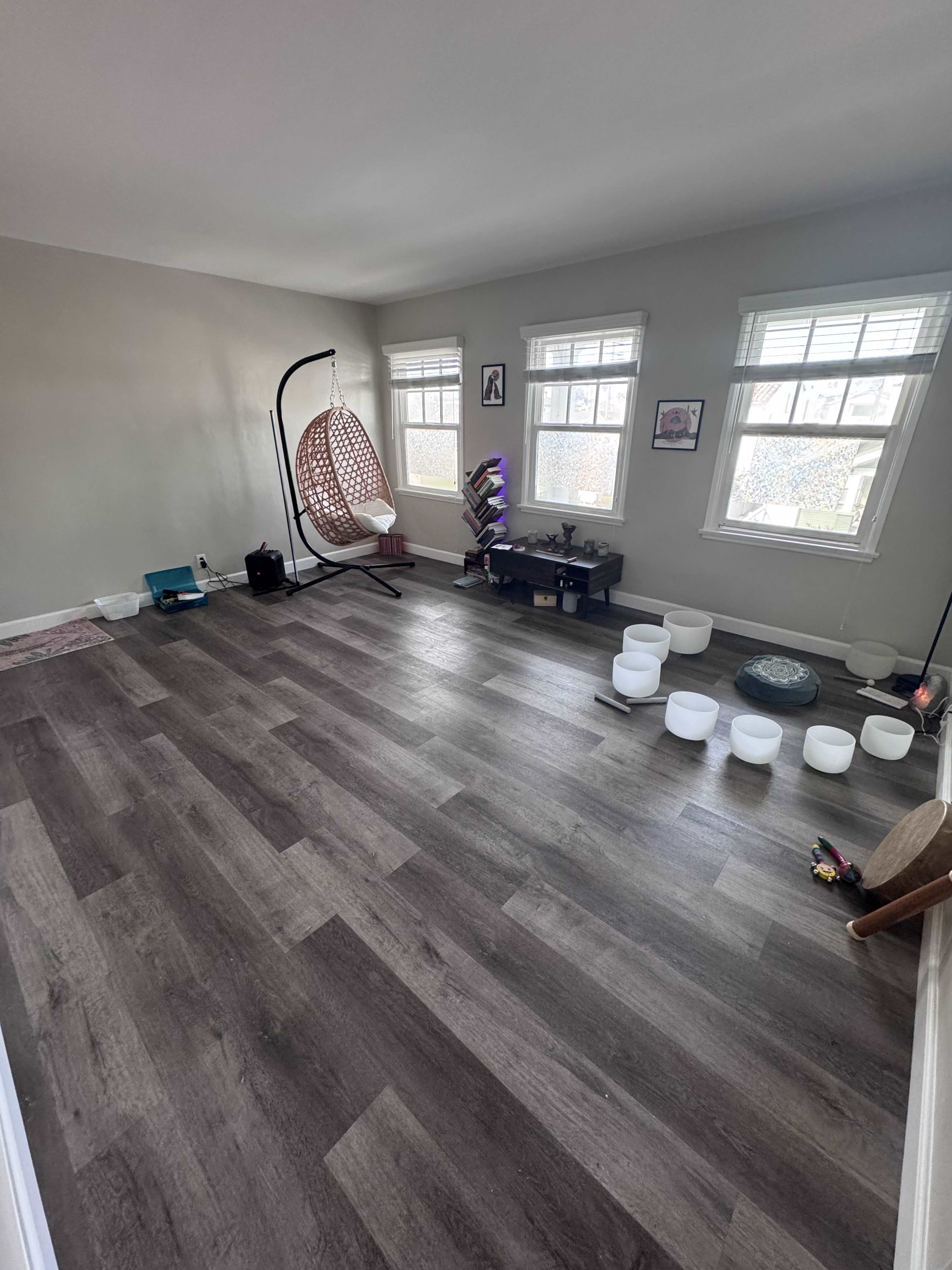 The image shows a spacious room with a hanging chair, several small white bowls arranged on the floor, and natural light coming through the windows.