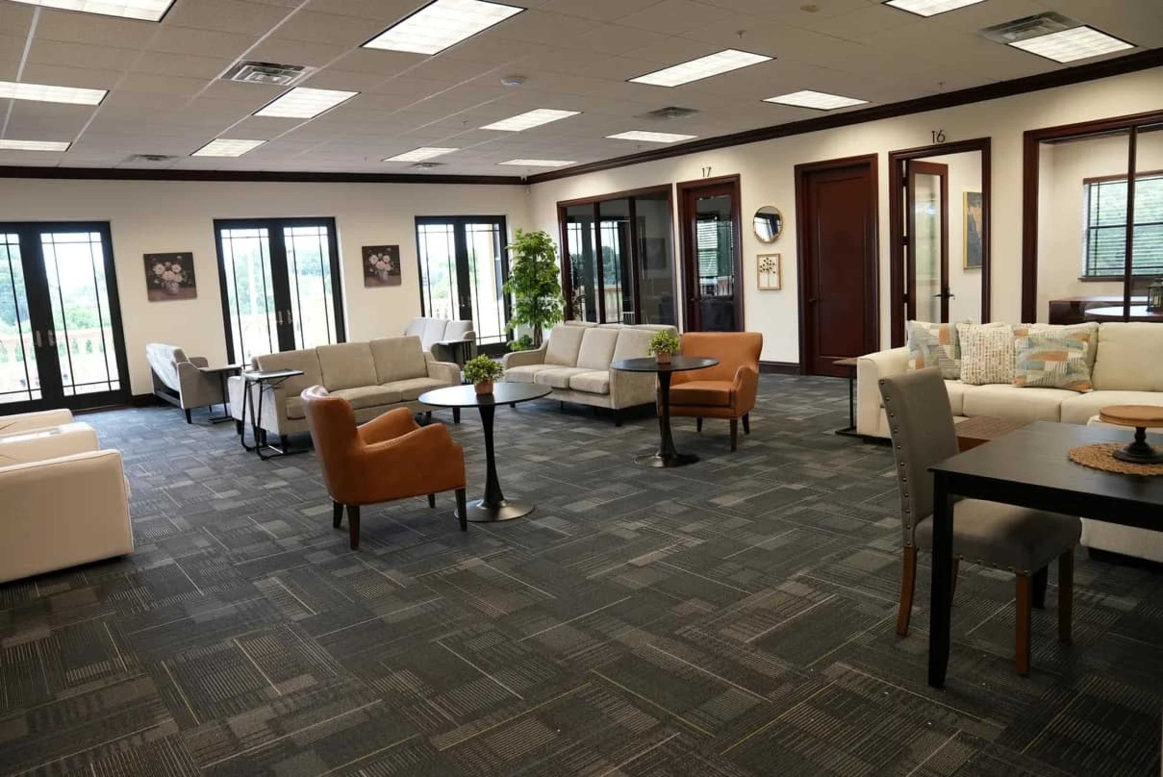 The image shows an office lounge area with multiple seating arrangements, including couches and chairs, surrounded by large windows.