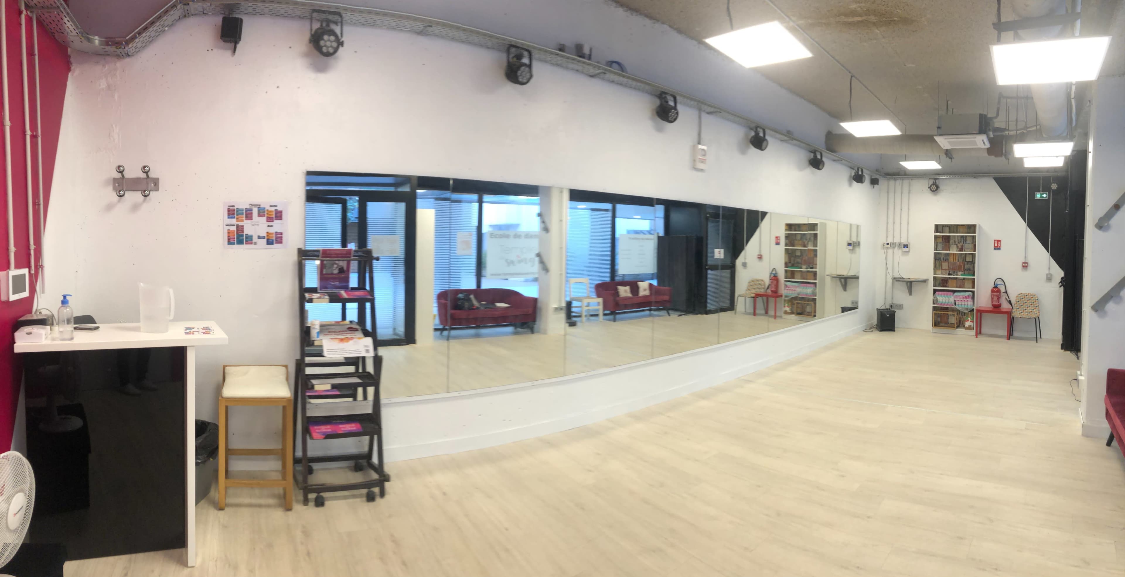 A spacious room with a large mirror on one wall, a small seating area, and shelves filled with items on the opposite side.