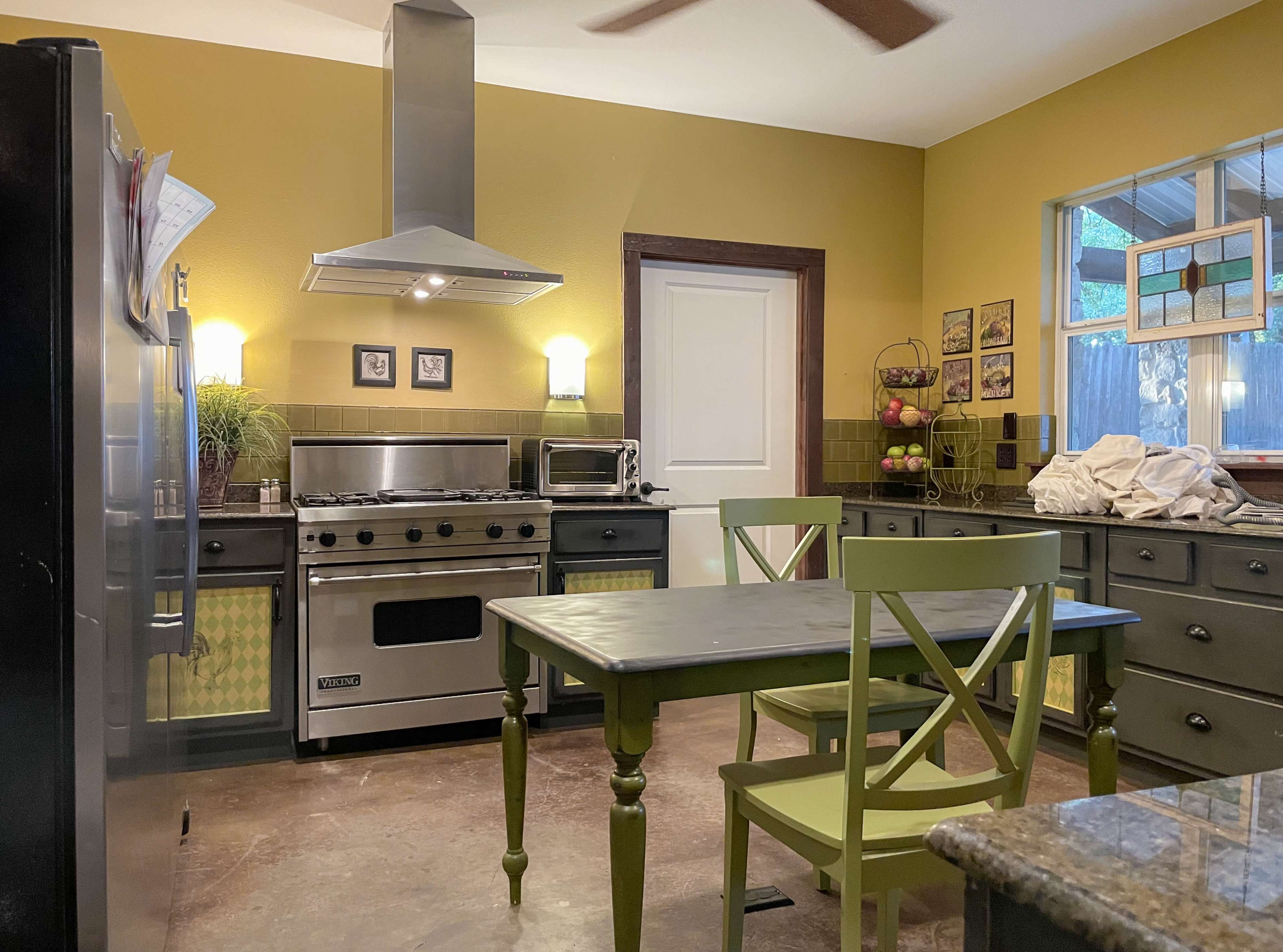 A modern kitchen features stainless steel appliances, a green dining set, and yellow walls.