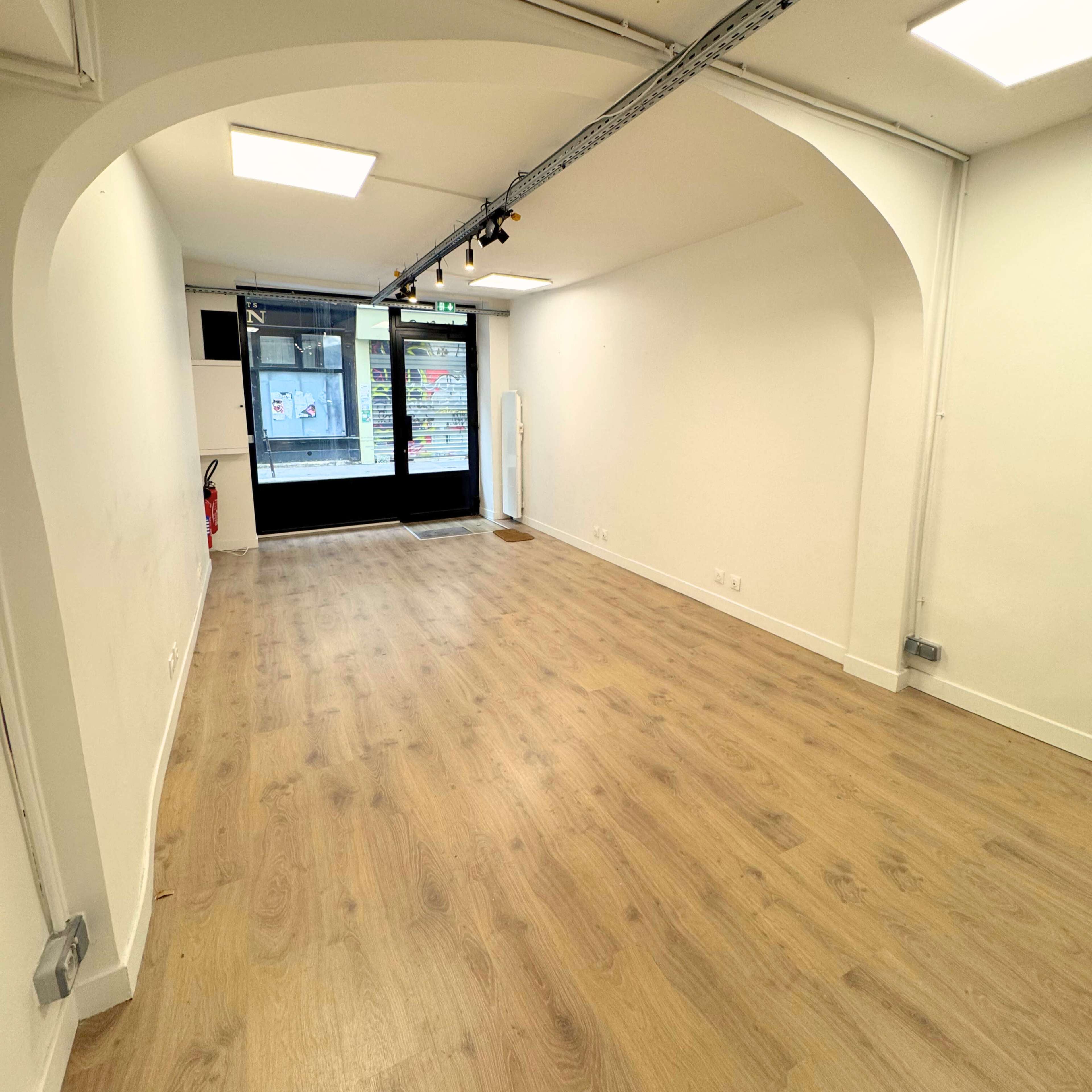 The image shows a spacious, empty retail space with wooden flooring and large windows at the front.