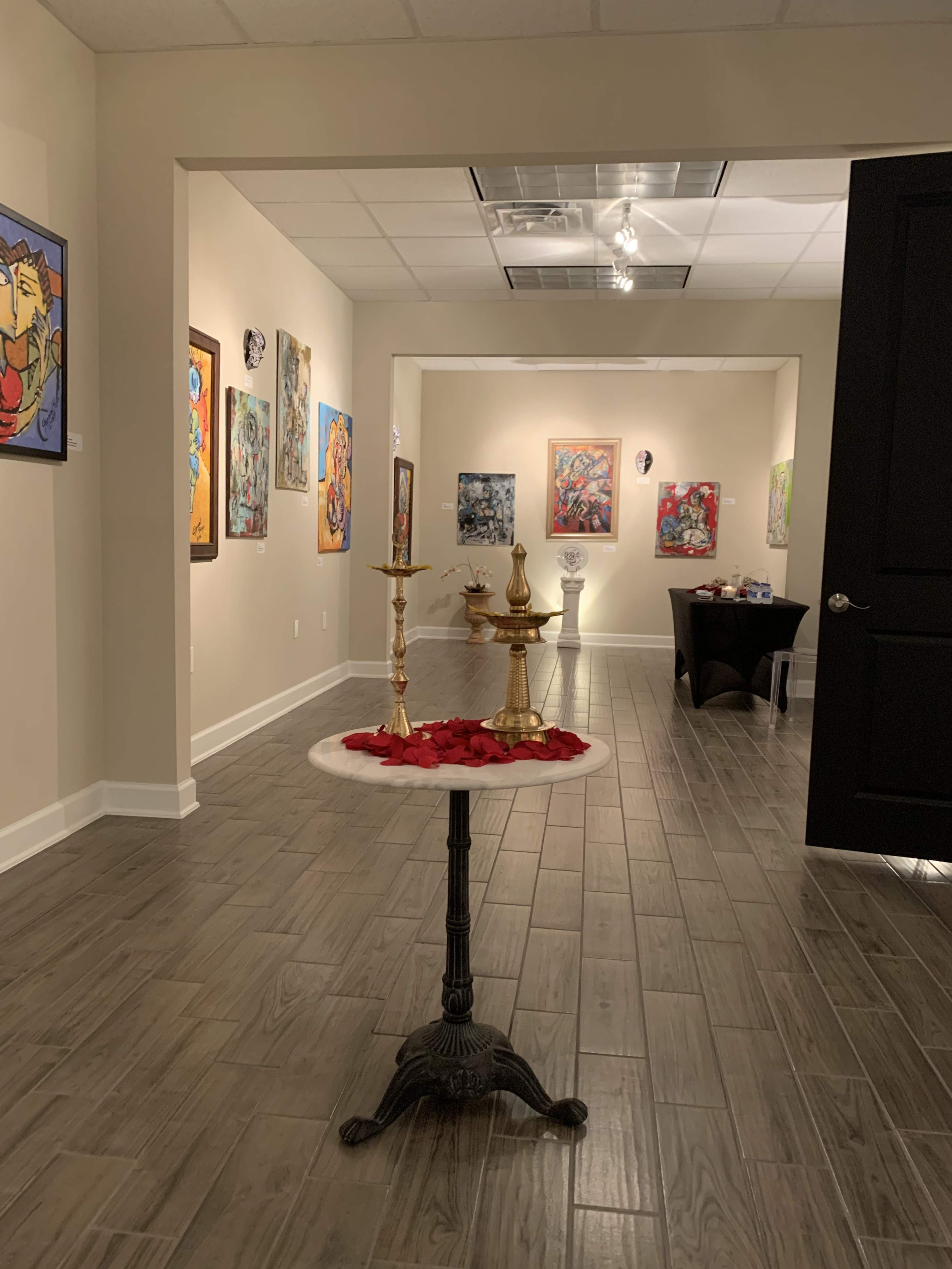 An art gallery with paintings displayed on the walls and a table in the foreground adorned with candles and rose petals.