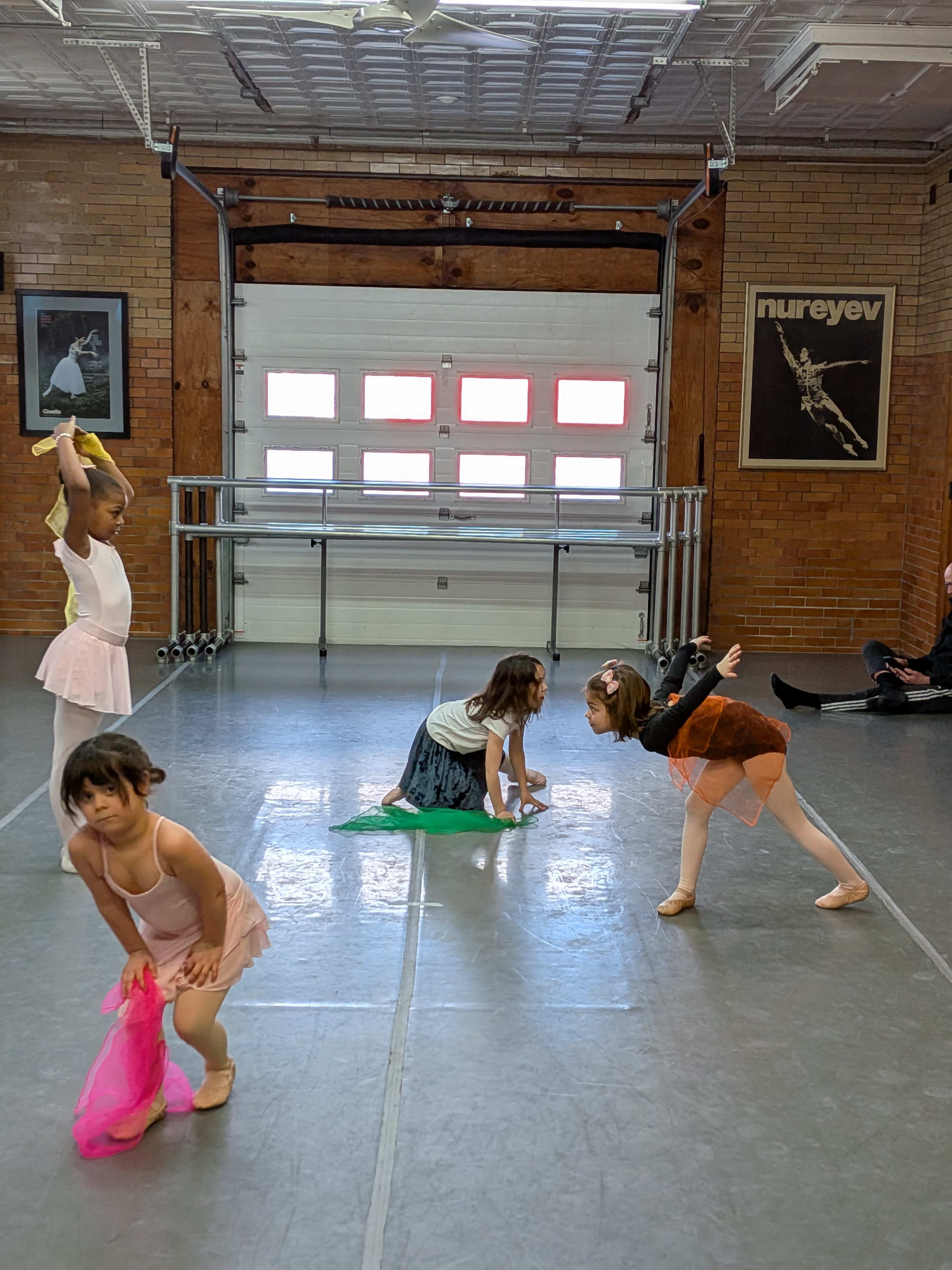 A group of young ballet dancers is practicing in a studio with mirrors and barre equipment.
