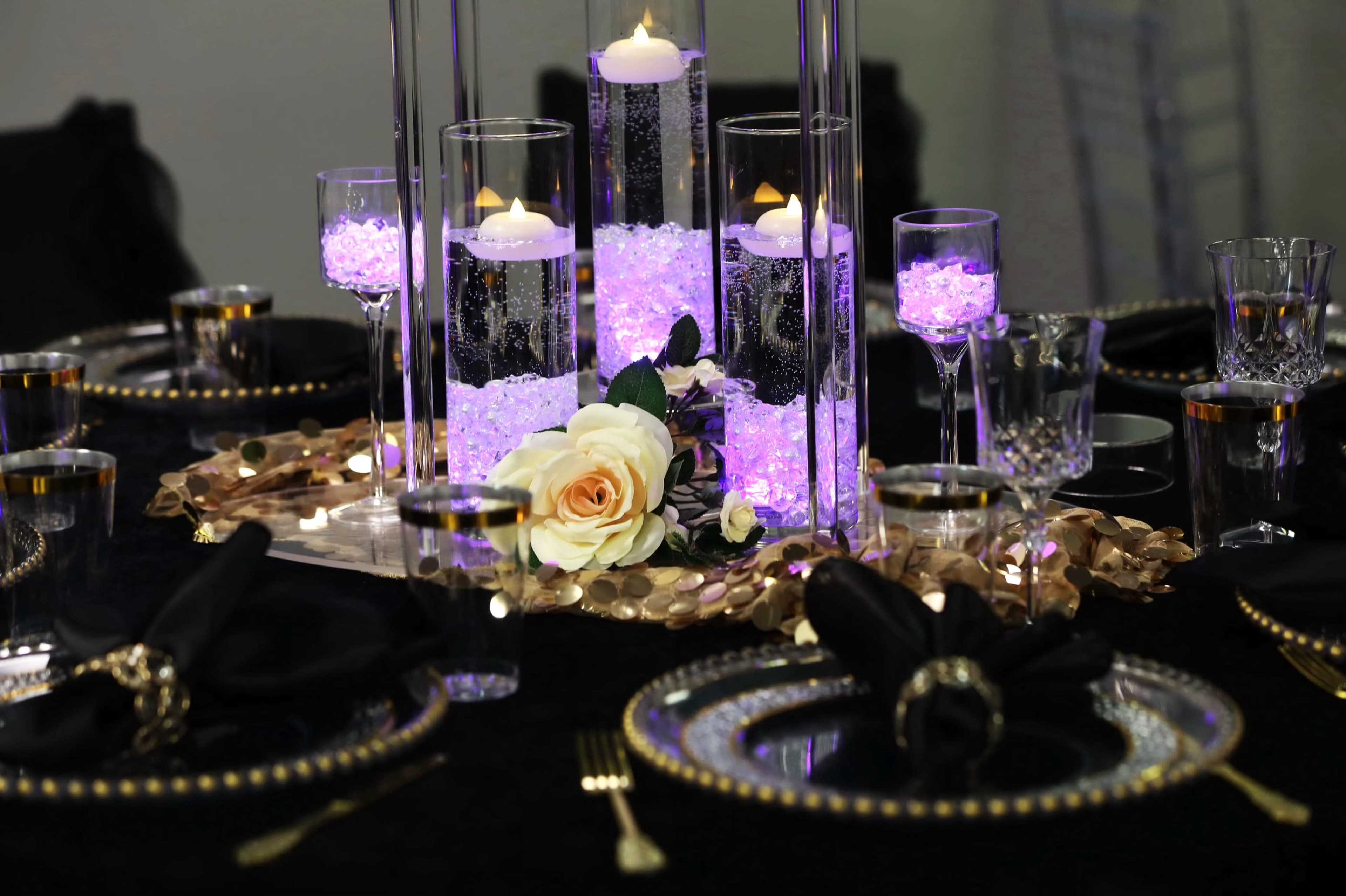 A beautifully arranged dinner table features crystal candle holders with floating candles, purple decorative stones, and elegant glassware.