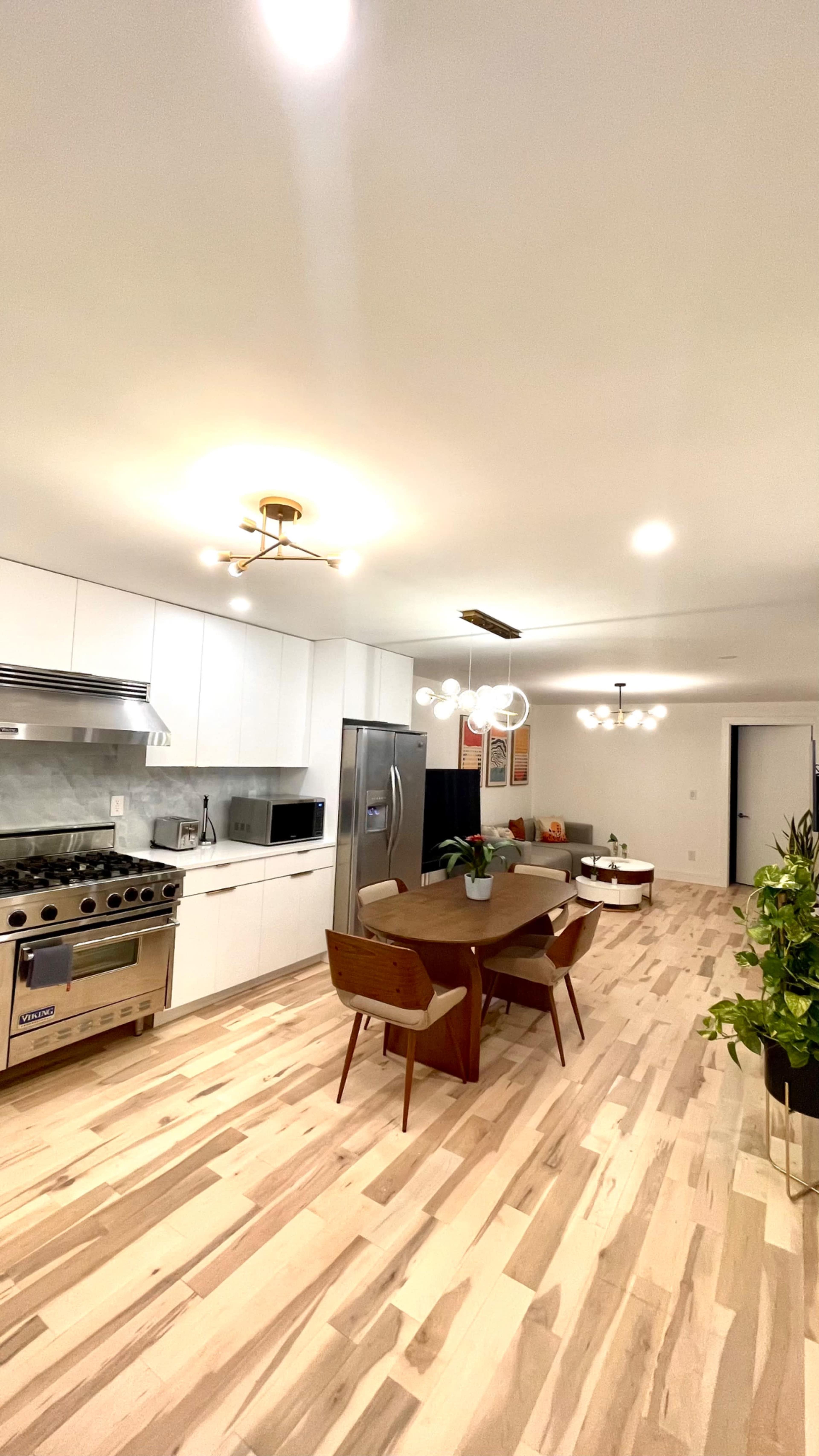 A modern kitchen and dining area featuring white cabinetry, stainless steel appliances, a round dining table, and wooden flooring.