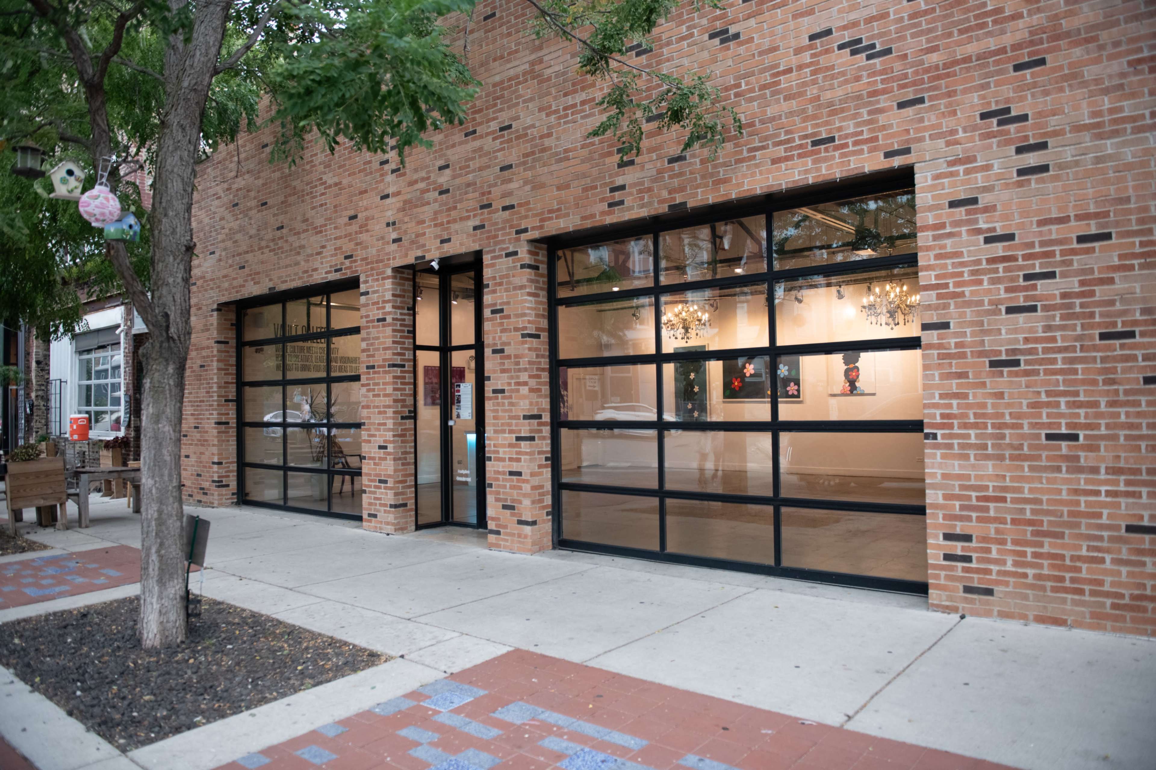 The image shows a brick facade with large glass windows and a sidewalk leading to the entrance of a commercial building.