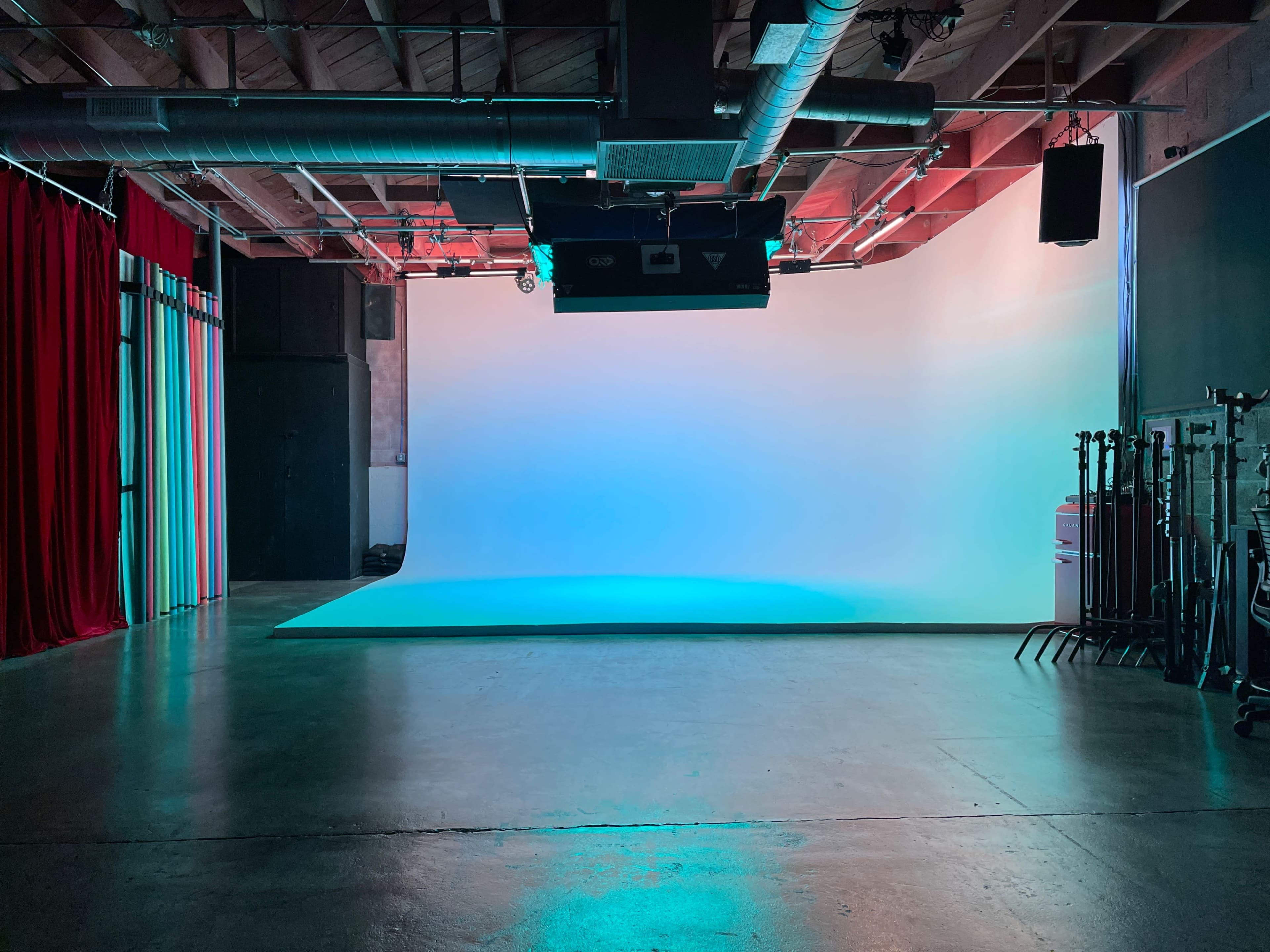 The image shows a photography studio with a seamless backdrop, featuring a clean, brightly lit space and green and red curtains on one side.