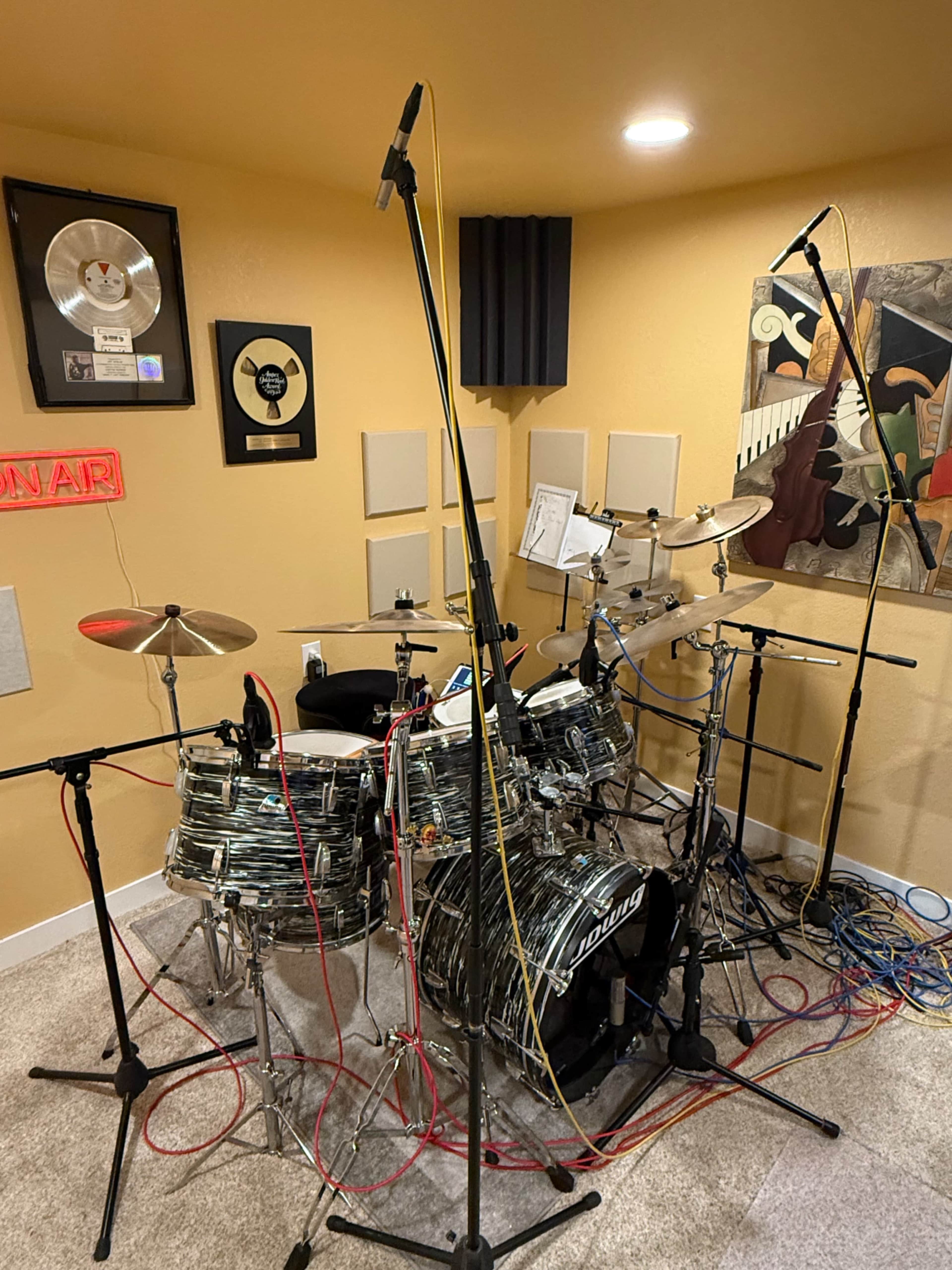 A well-equipped drumming studio features a set of drums surrounded by microphones, various soundproofing panels, and music awards on the walls.