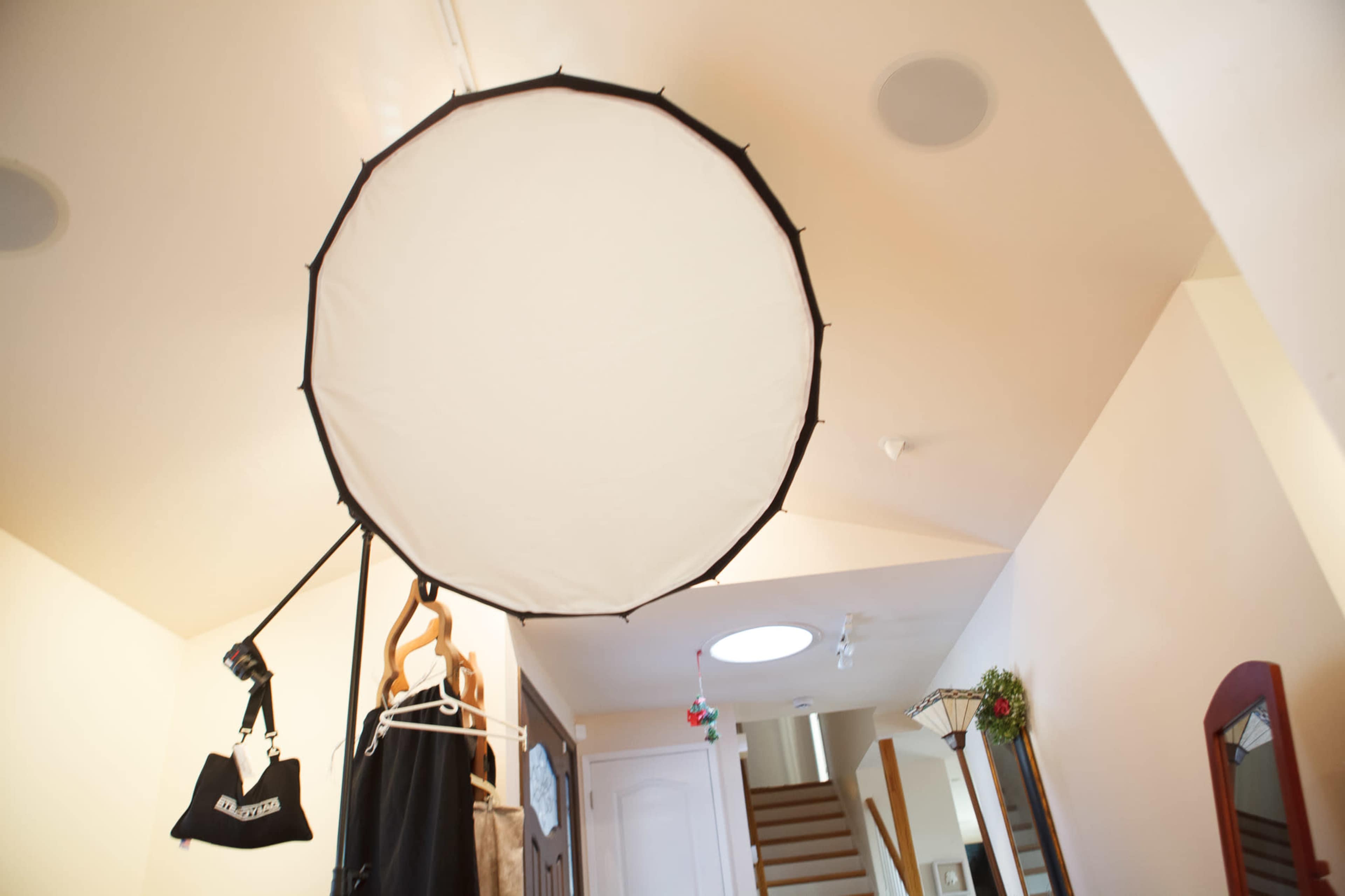 A large circular softbox is suspended from the ceiling in a well-lit entryway with a staircase visible in the background.