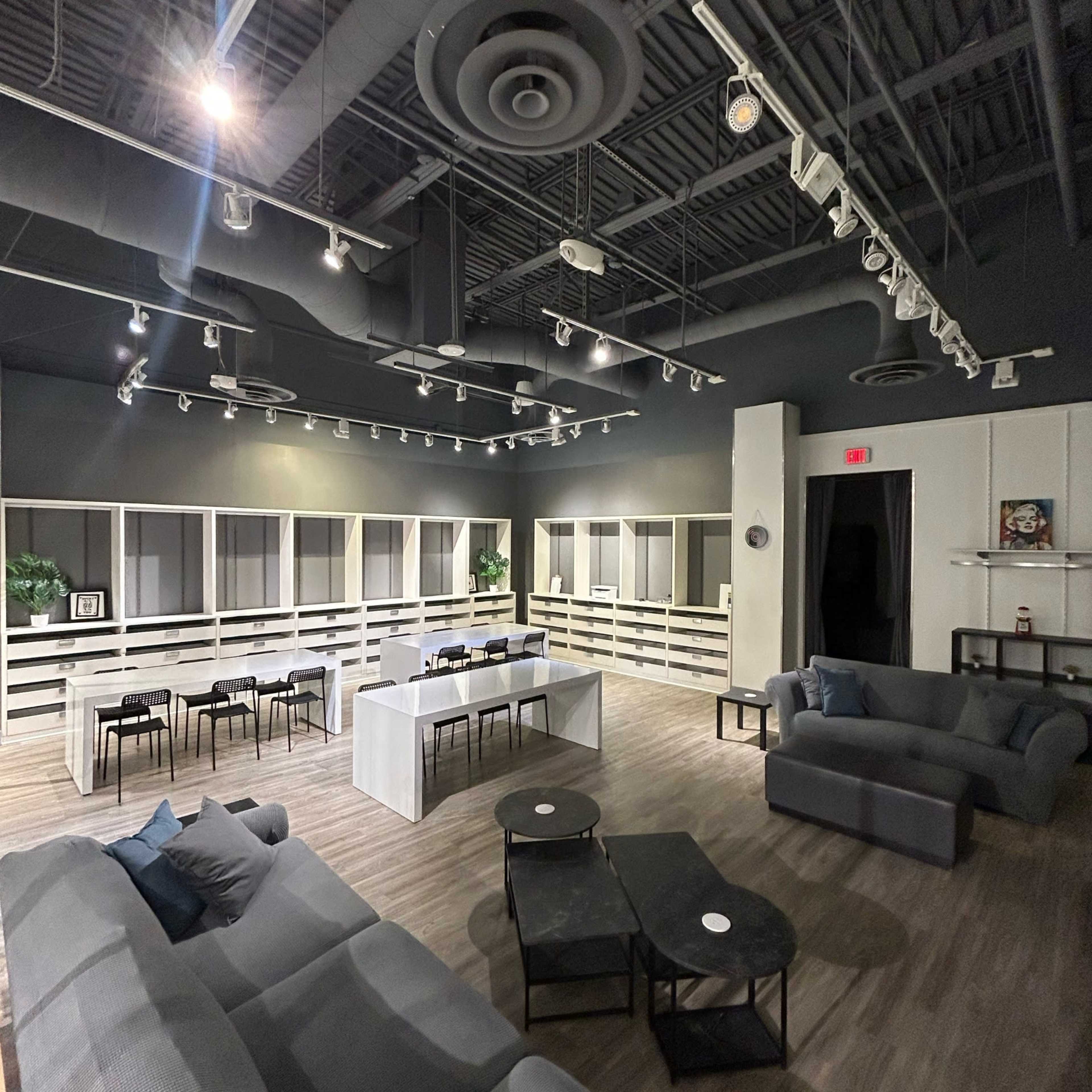 The image shows a spacious, modern lounge area with several seating arrangements, including sofas and tables, and shelves lining the walls.