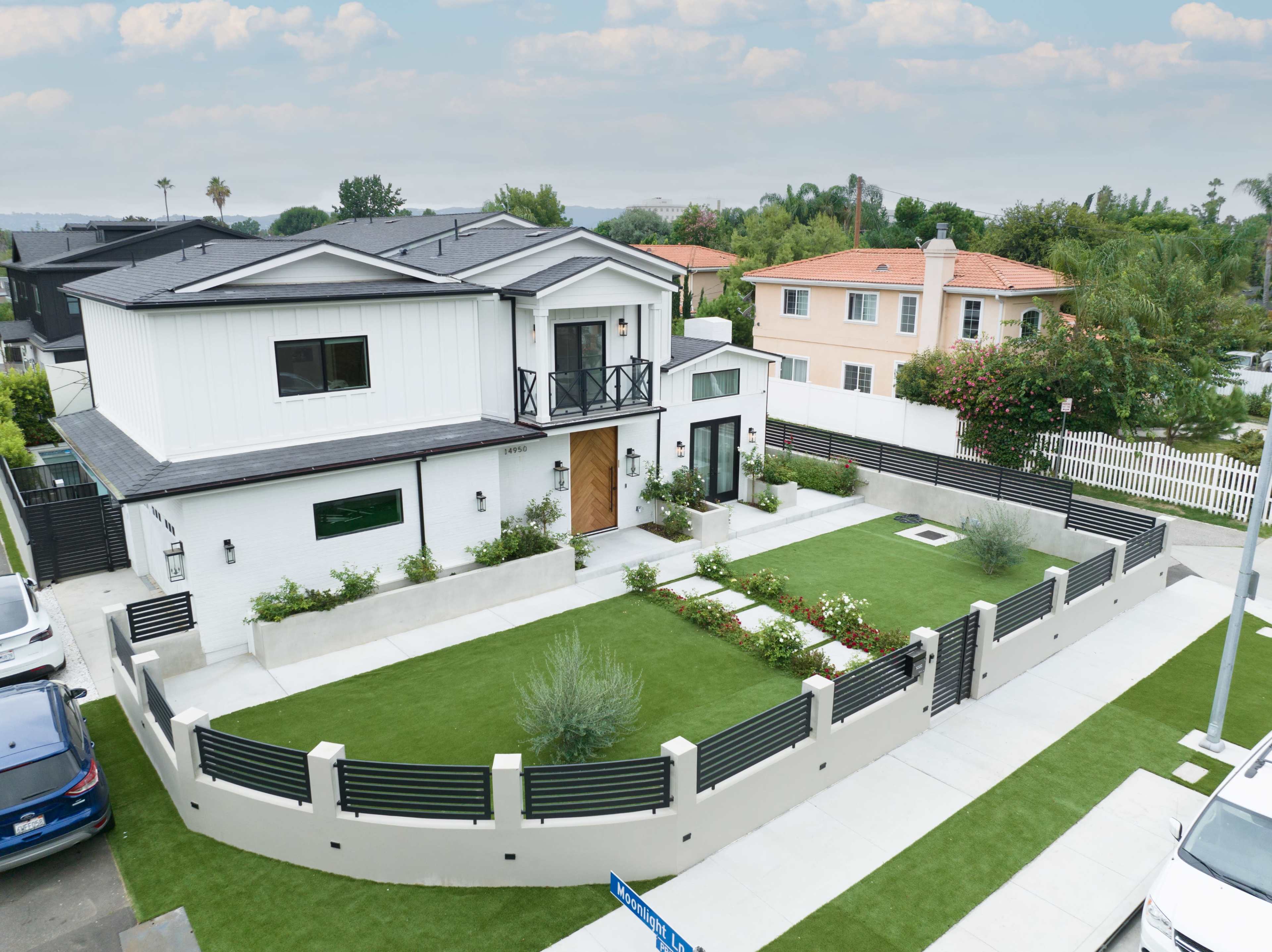 A large, modern two-story house with a white exterior, surrounded by a landscaped yard featuring green grass and flower beds.