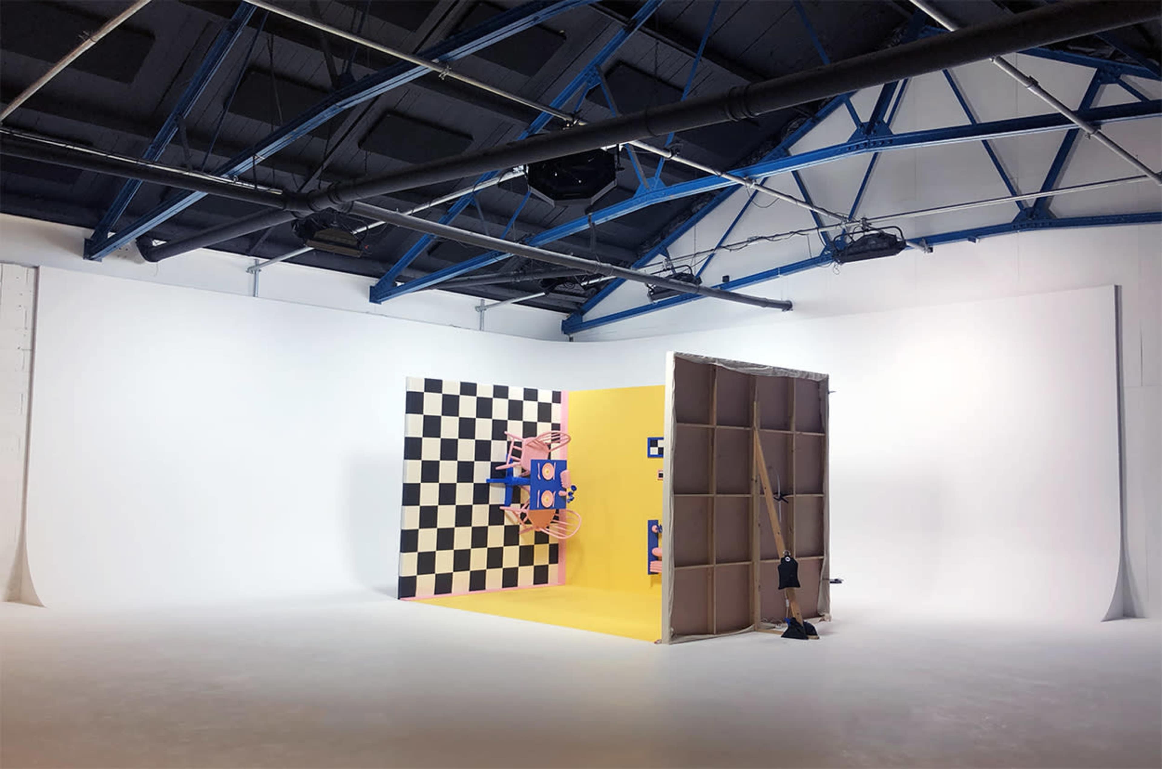 A spacious studio with a white backdrop, a checkerboard wall, and a brightly colored yellow wall featuring playful designs.