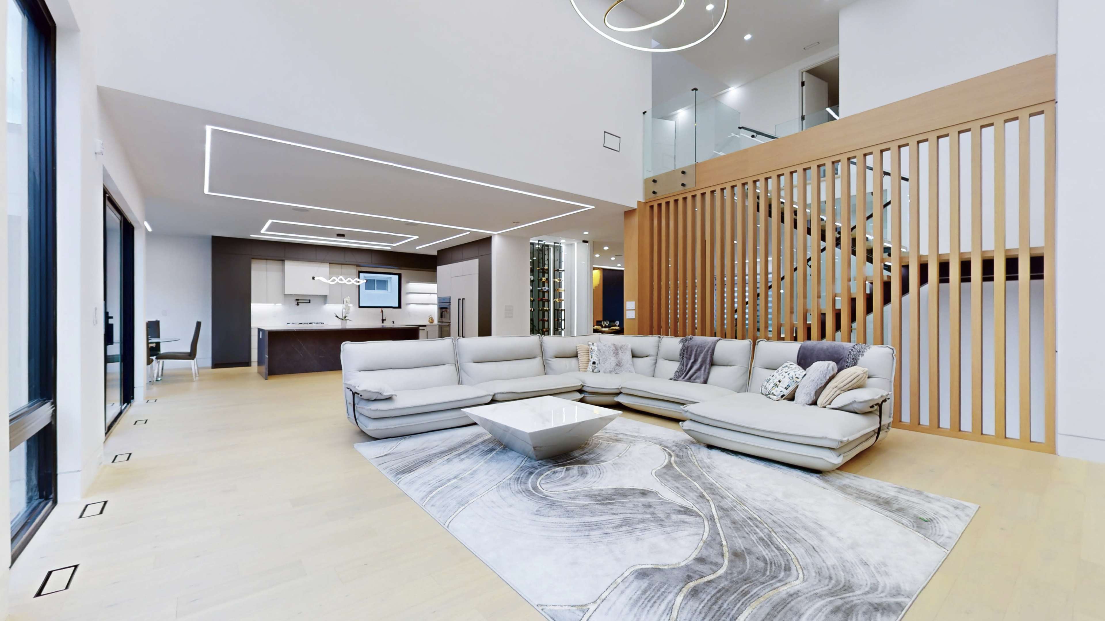 A spacious living room featuring a large sectional sofa, a central coffee table, a patterned rug, and a staircase with wooden accents.