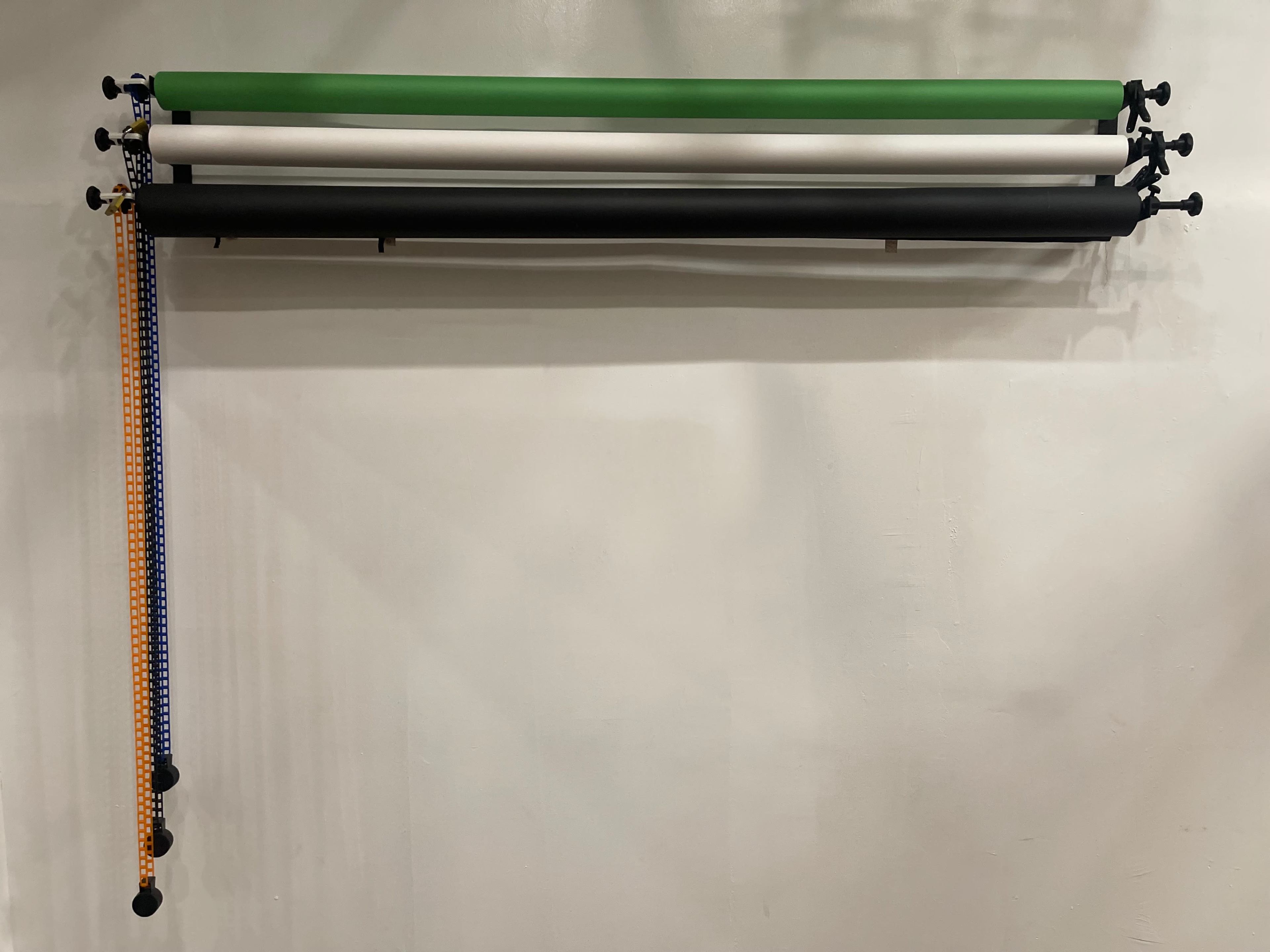 A wall-mounted rack holding four rolls of different colored materials, with a patterned strap hanging down on one side.