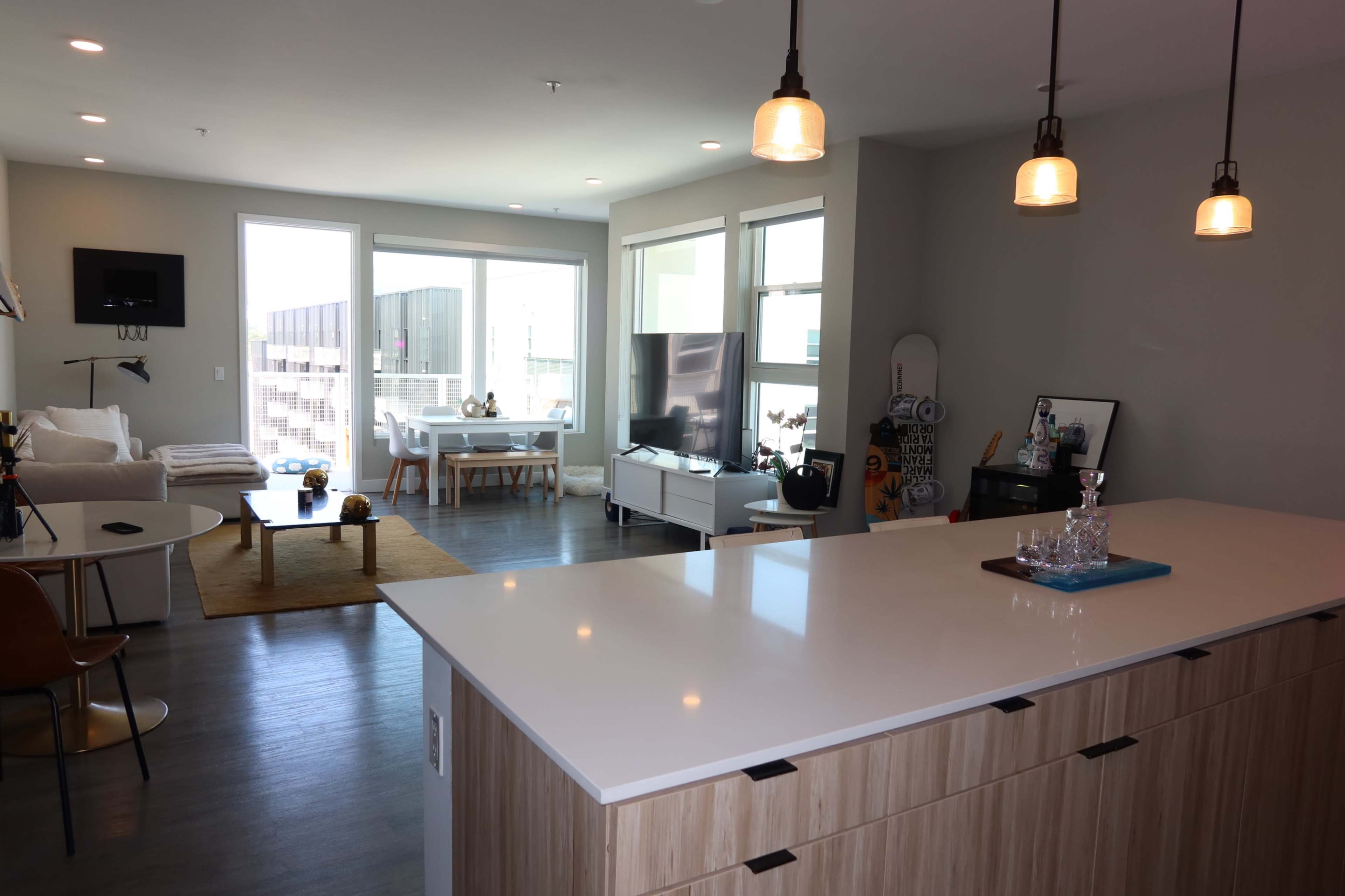 A modern open-concept living space features a kitchen island, dining area, and a living room with large windows and contemporary furnishings.