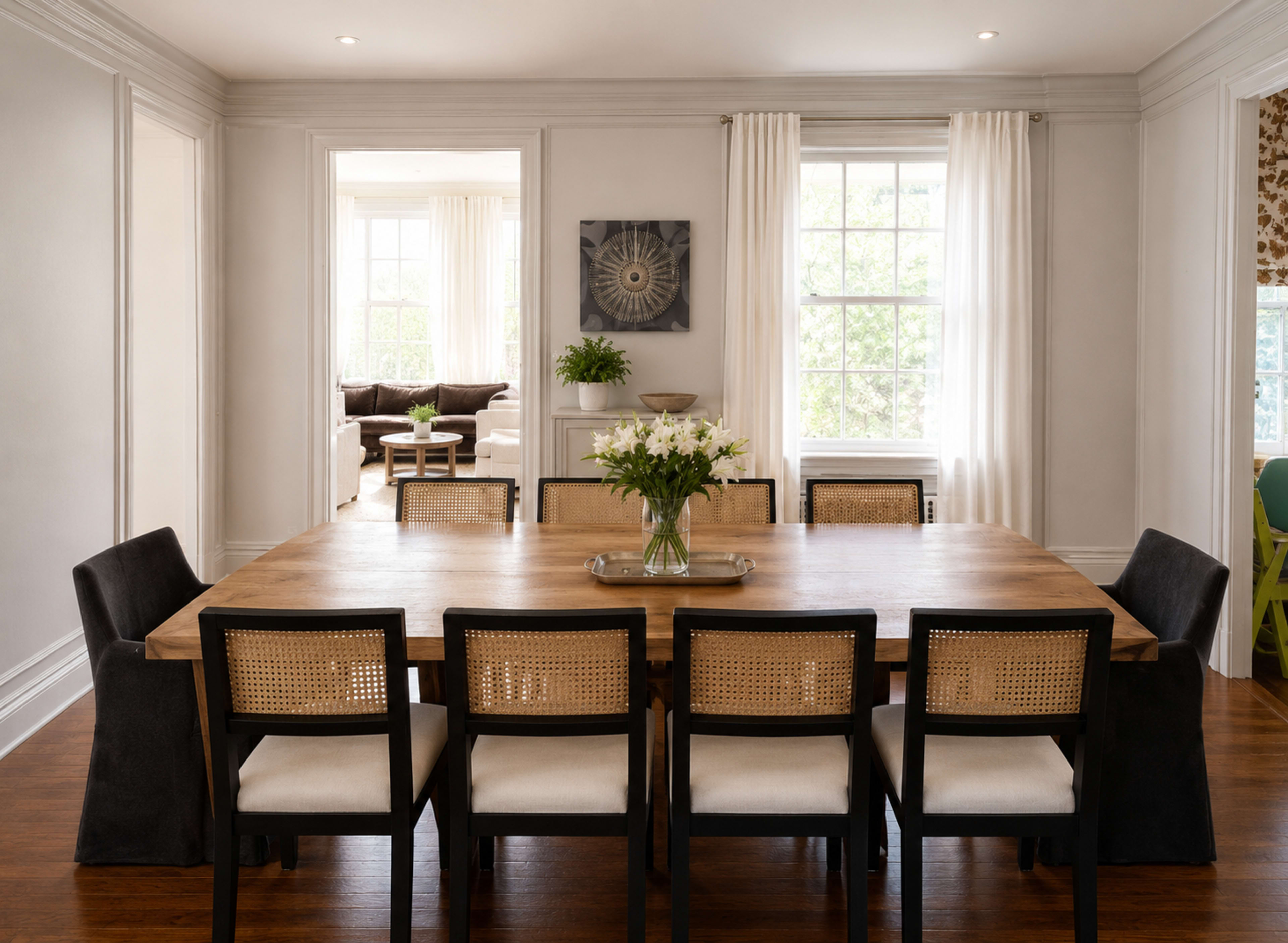 A large wooden dining table is surrounded by eight black and white chairs in a bright, airy dining room.