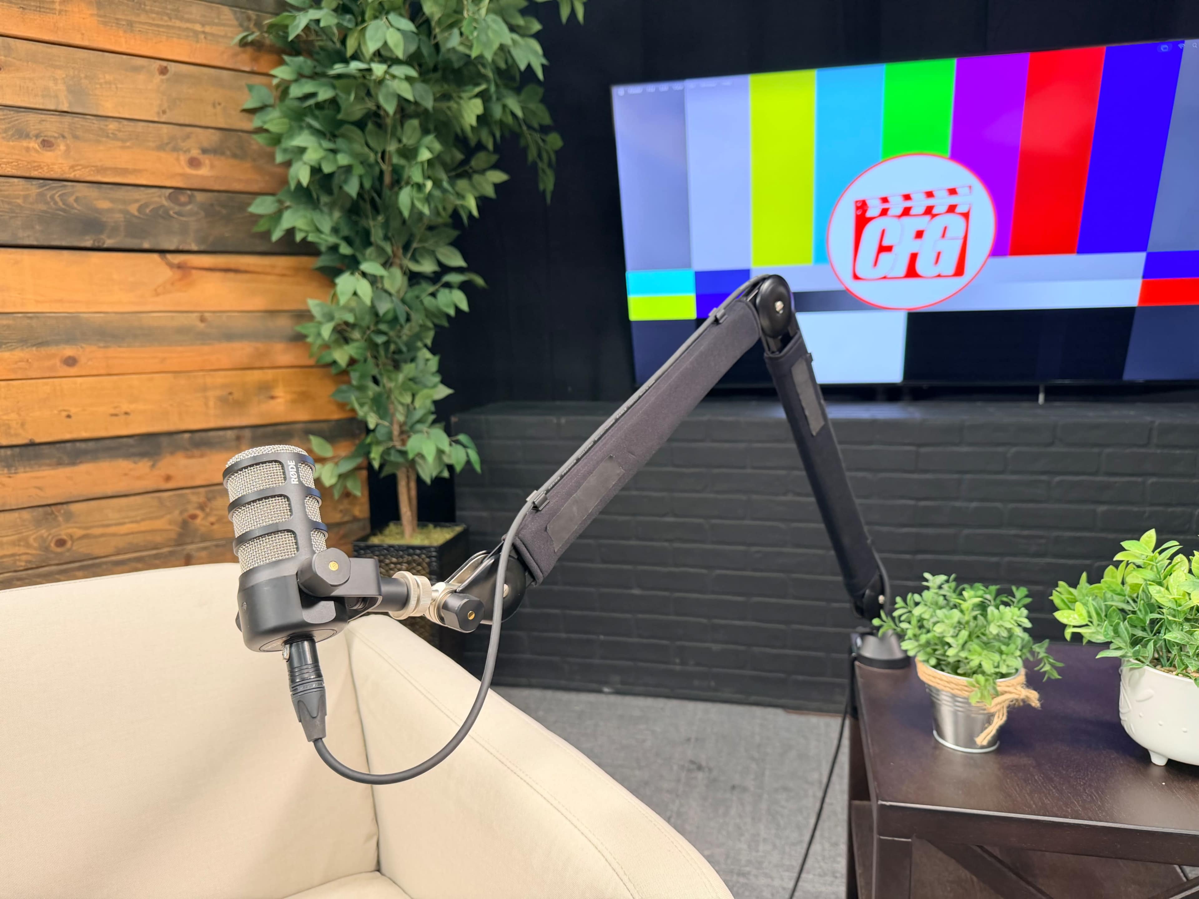A microphone is mounted on an adjustable arm beside a couch in front of a television displaying a color test pattern.