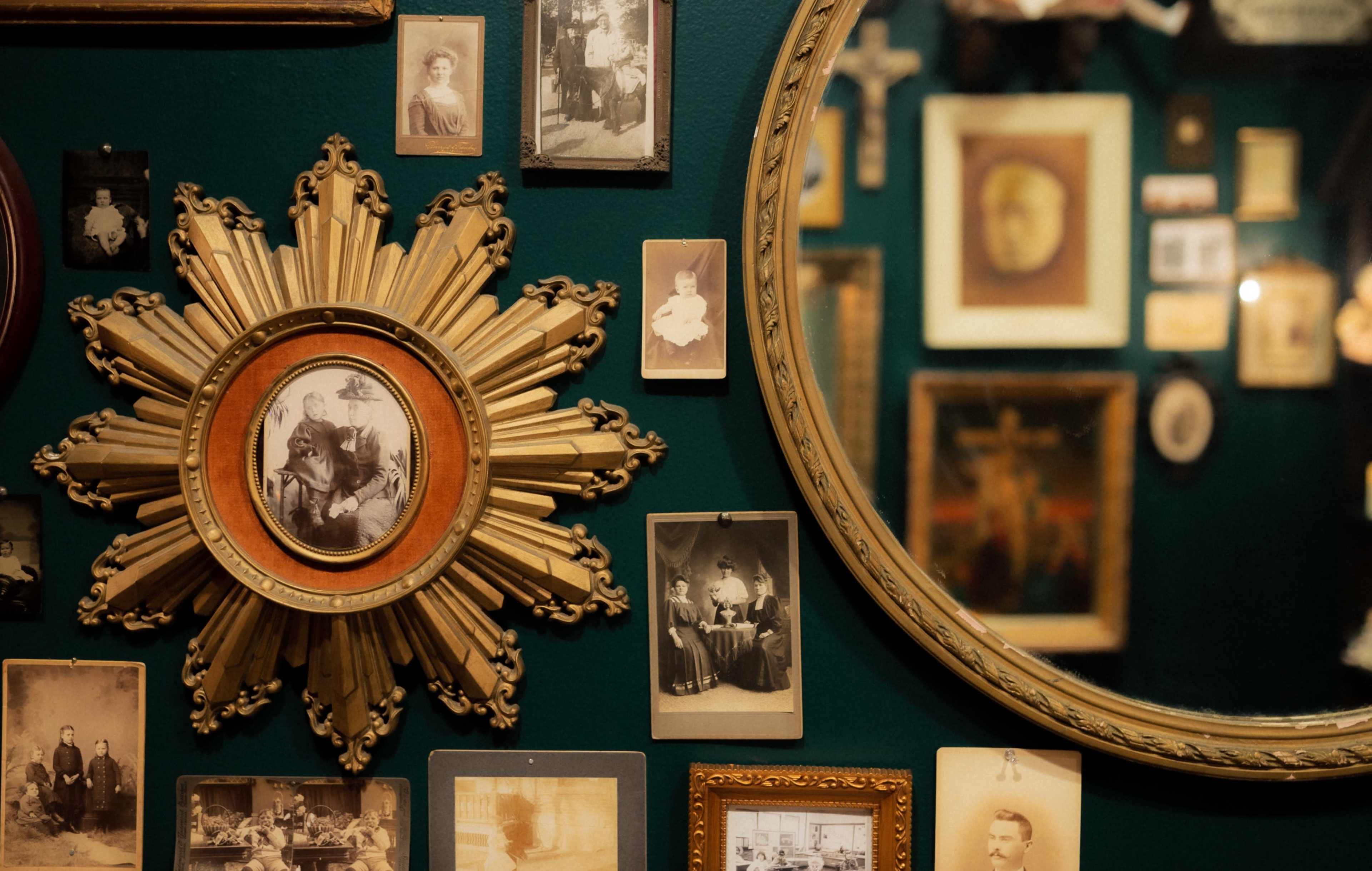 A gallery wall features a variety of vintage photographs arranged around a decorative sunburst mirror.