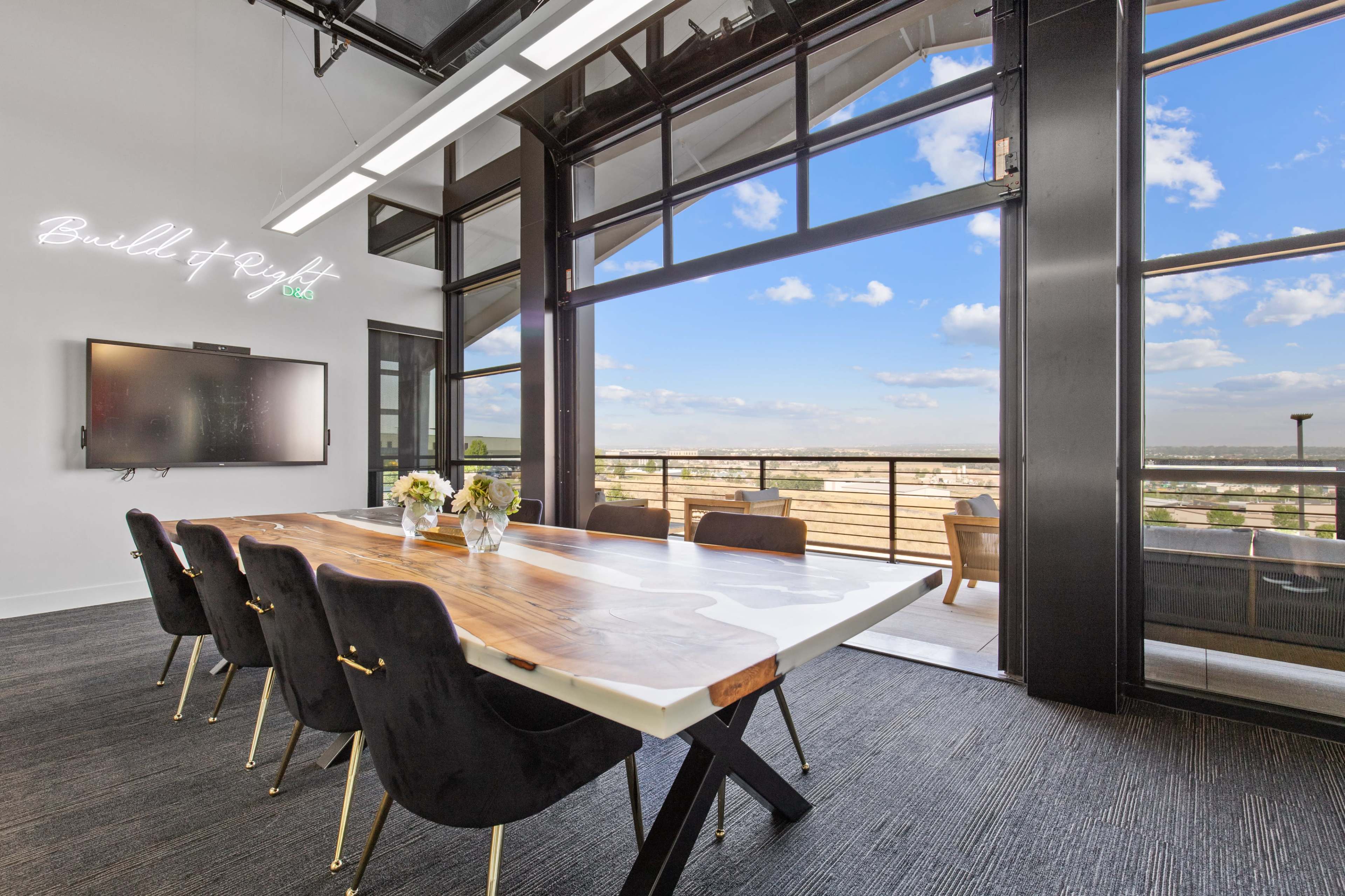 A modern conference room features a wooden table surrounded by black chairs, with large windows offering a panoramic view of the cityscape.